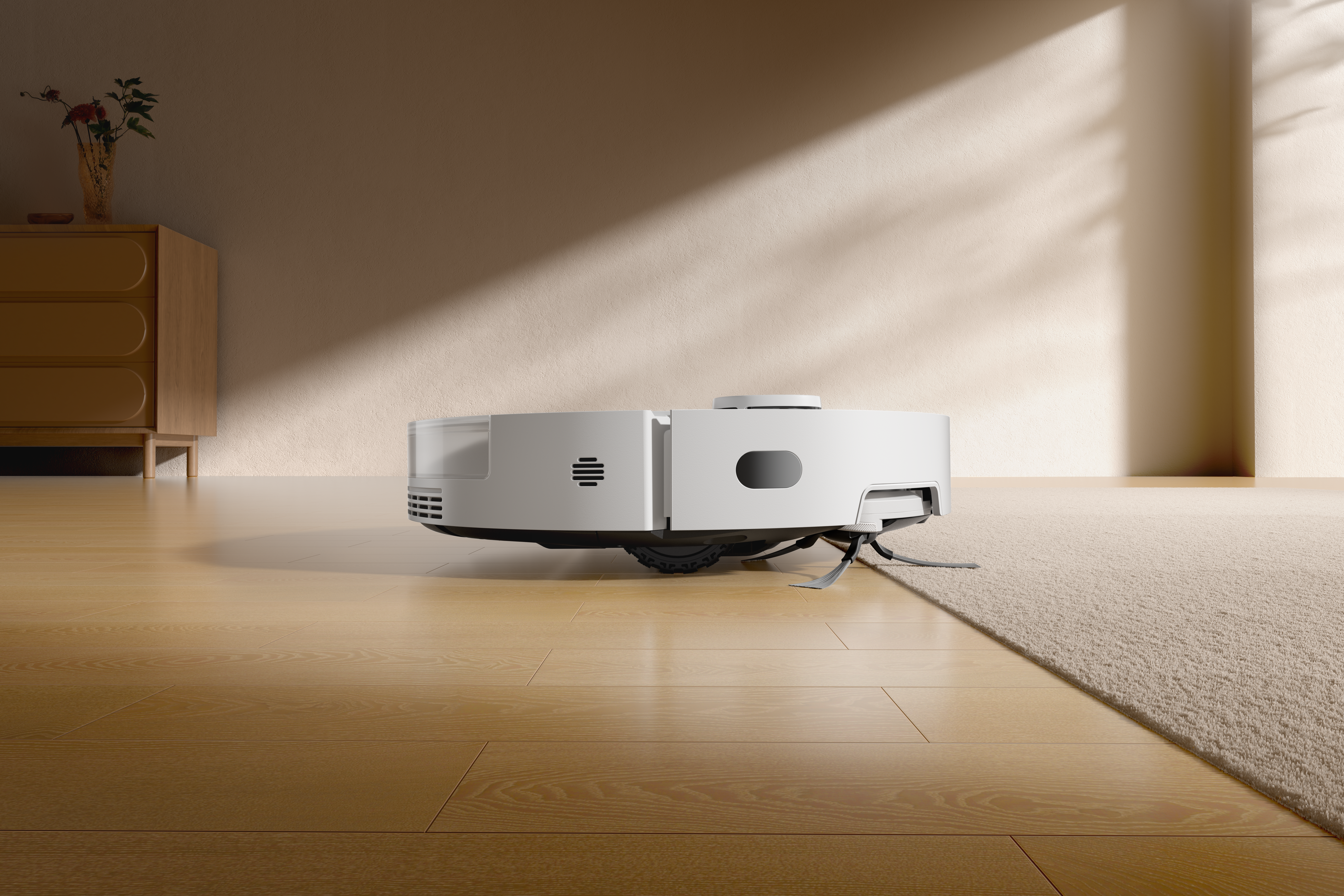 Biały robot sprzątający na drewnianej podłodze. Szafka z kwiatami po lewej, dywan po prawej.