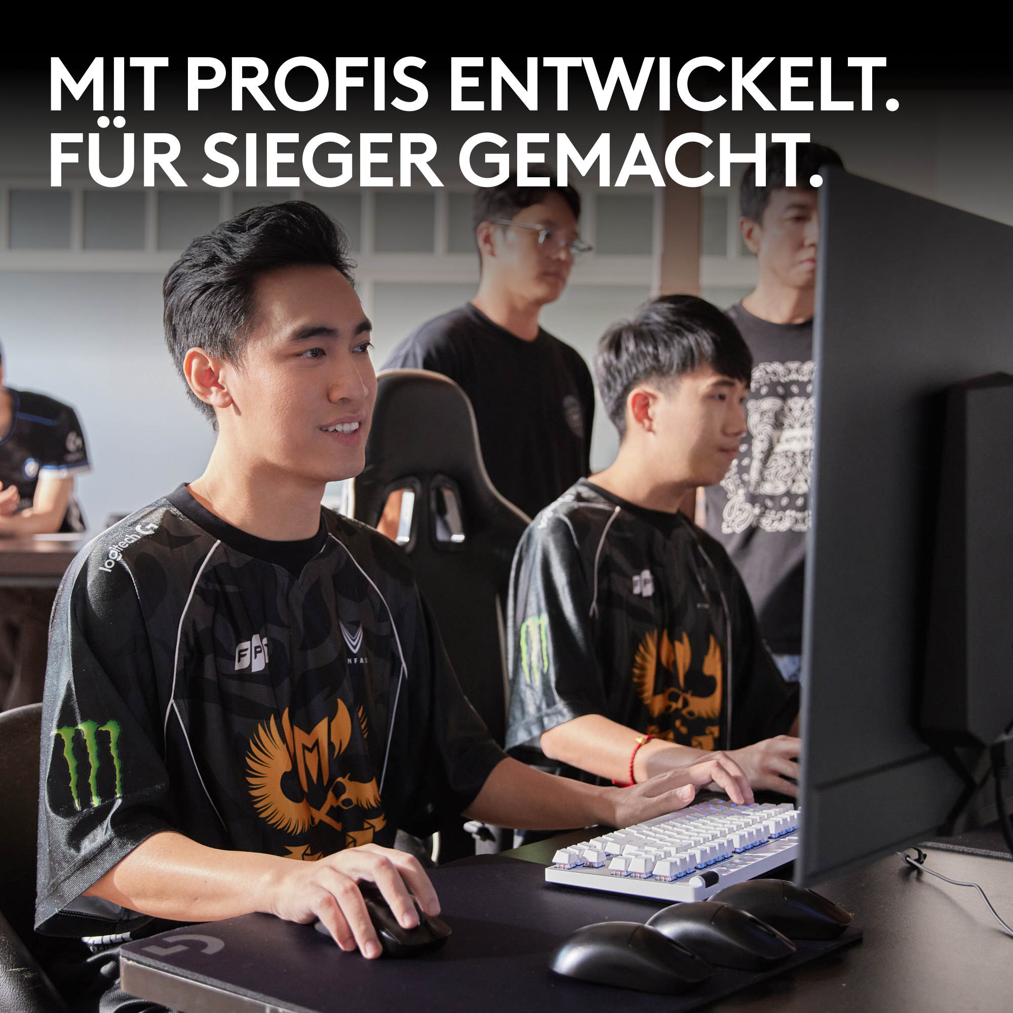 Zwei junge Männer in Trikots spielen. Einer benutzt eine Maus, der andere eine Tastatur. Mehrere Personen sind im Hintergrund.
