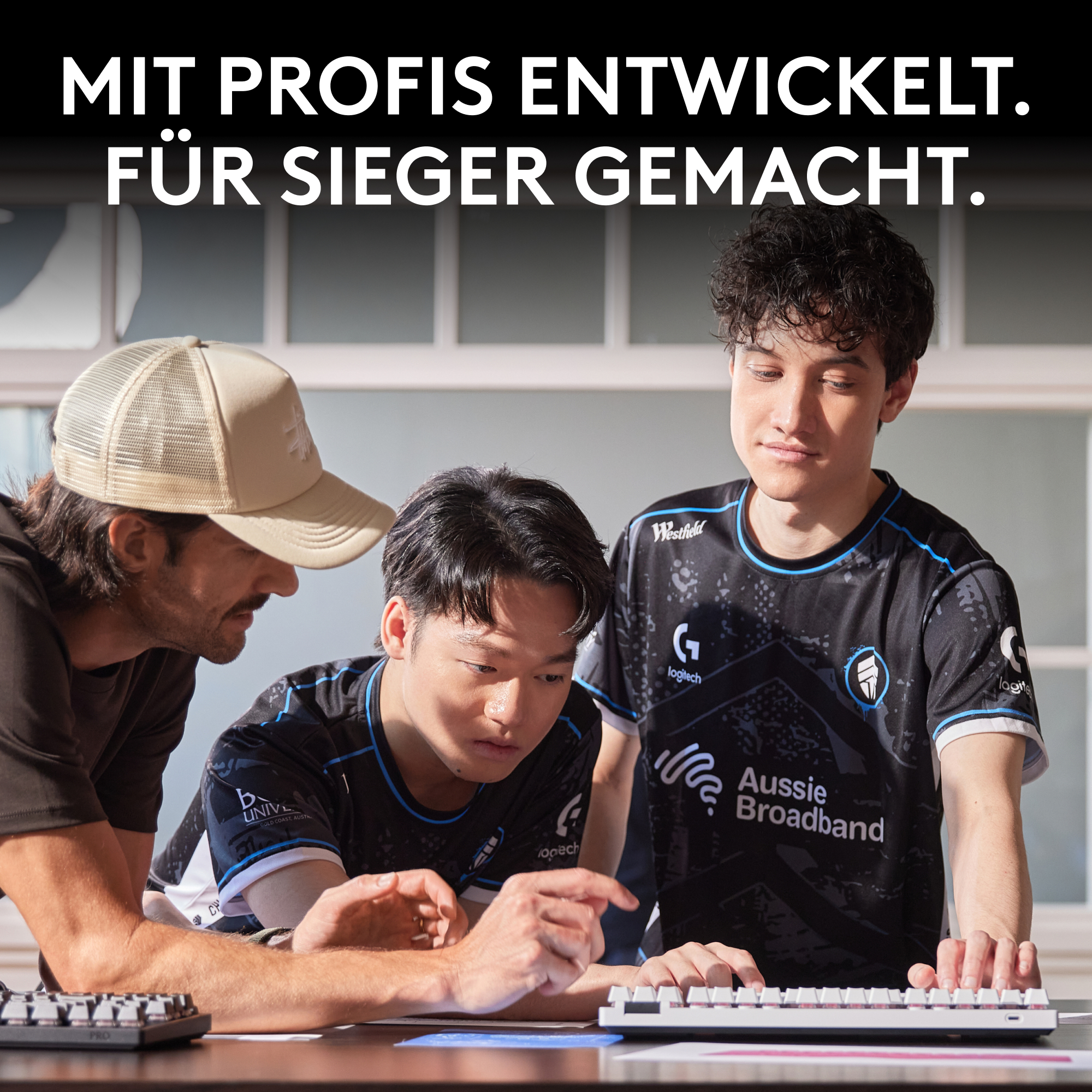 Drei Männer betrachten eine Tastatur. Einer trägt einen Hut. Zwei andere tragen schwarze Trikots. Der Text lautet 'Mit Profis Entwickelt'.