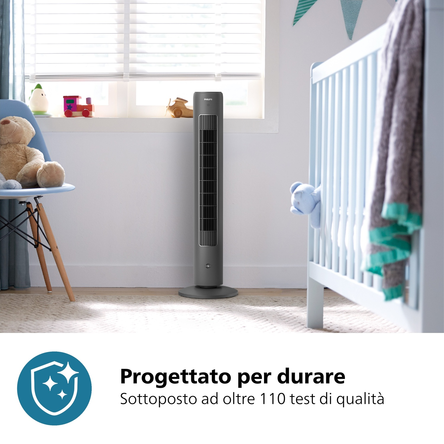 Un ventilatore a torre grigio si trova in una cameretta con una culla. I giocattoli sono sul davanzale. Un orsacchiotto è su una sedia.