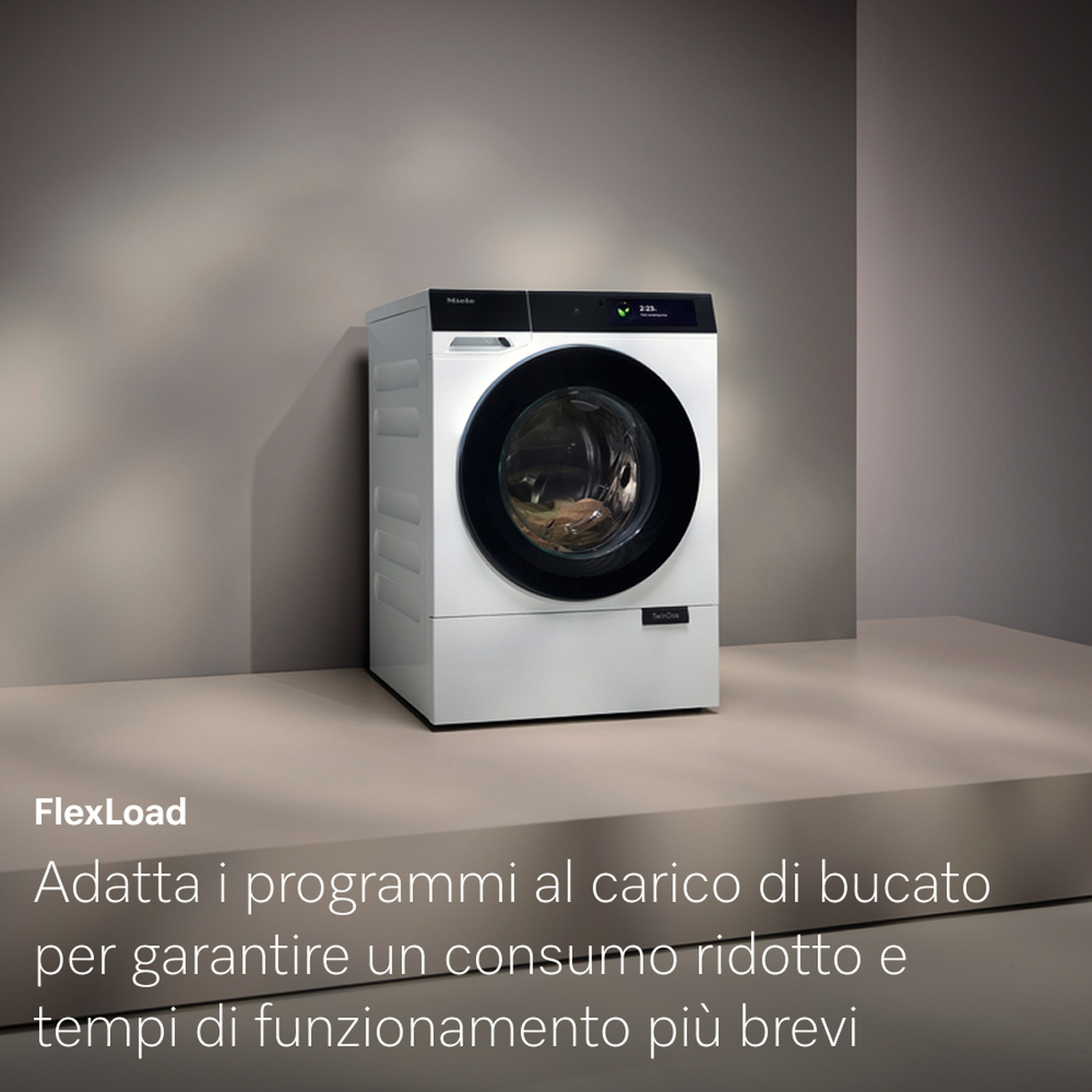 Una lavatrice Miele bianca con porta nera è centrata su sfondo grigio. Il testo dice FlexLoad e testo italiano sotto.