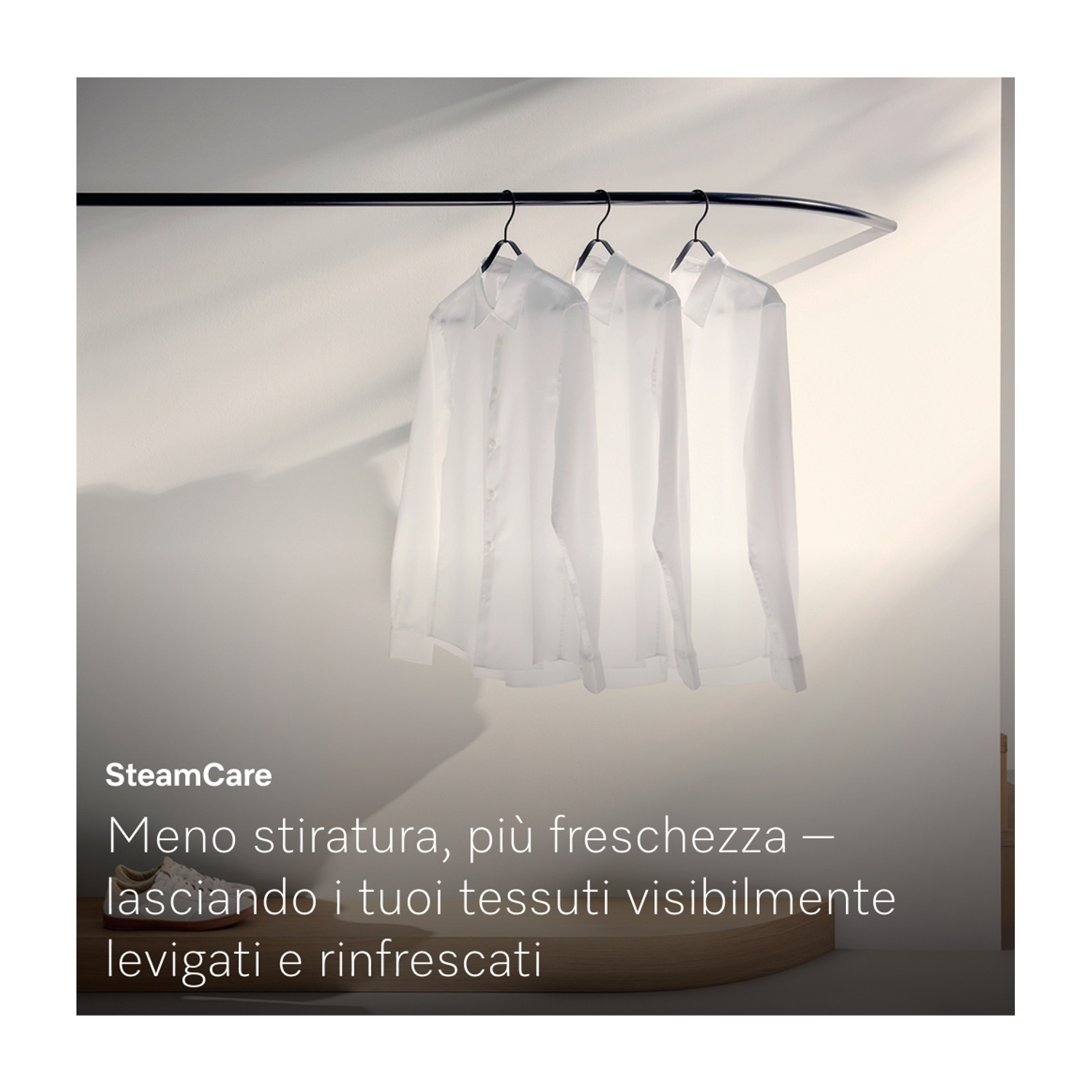 Tre camicie bianche appese a un'asta nera curva. Gioco di ombre sul muro. Testo SteamCare in basso nell'immagine.