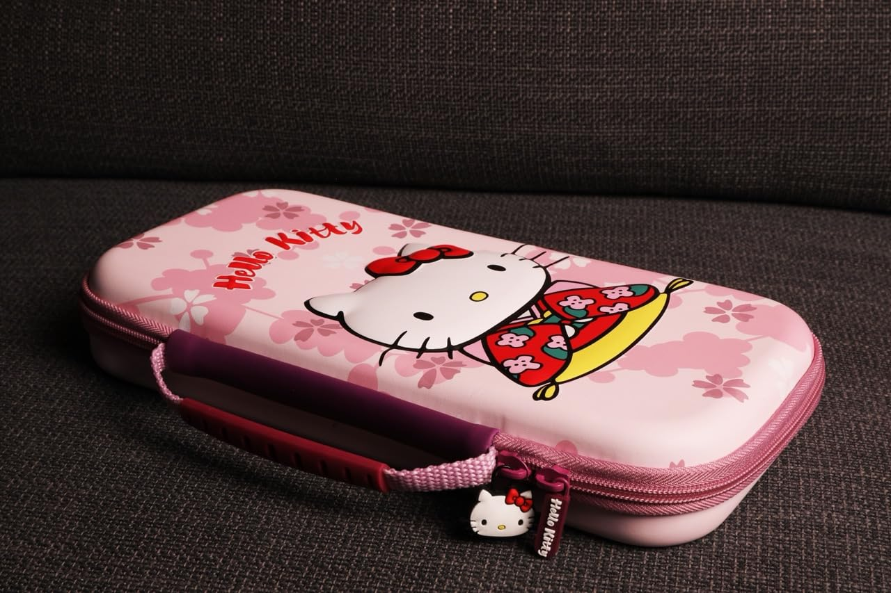 Un estuche rosa de Hello Kitty con flores de cerezo. El estuche tiene un tirador de cremallera de Hello Kitty y un asa morada. Descansa sobre una superficie gris.