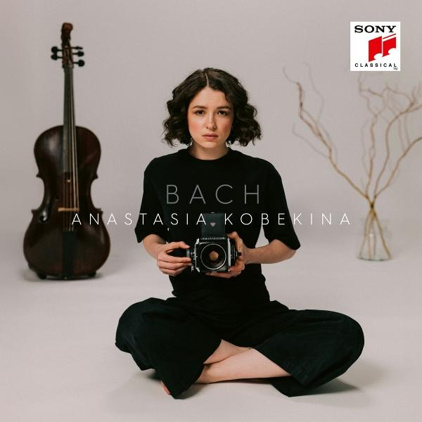 Frau mit Kamera, sitzt mit Cello. Text auf Shirt: 'BACH ANSTASIA KOBEKINA'. SONY CLASSICAL Logo oben rechts.