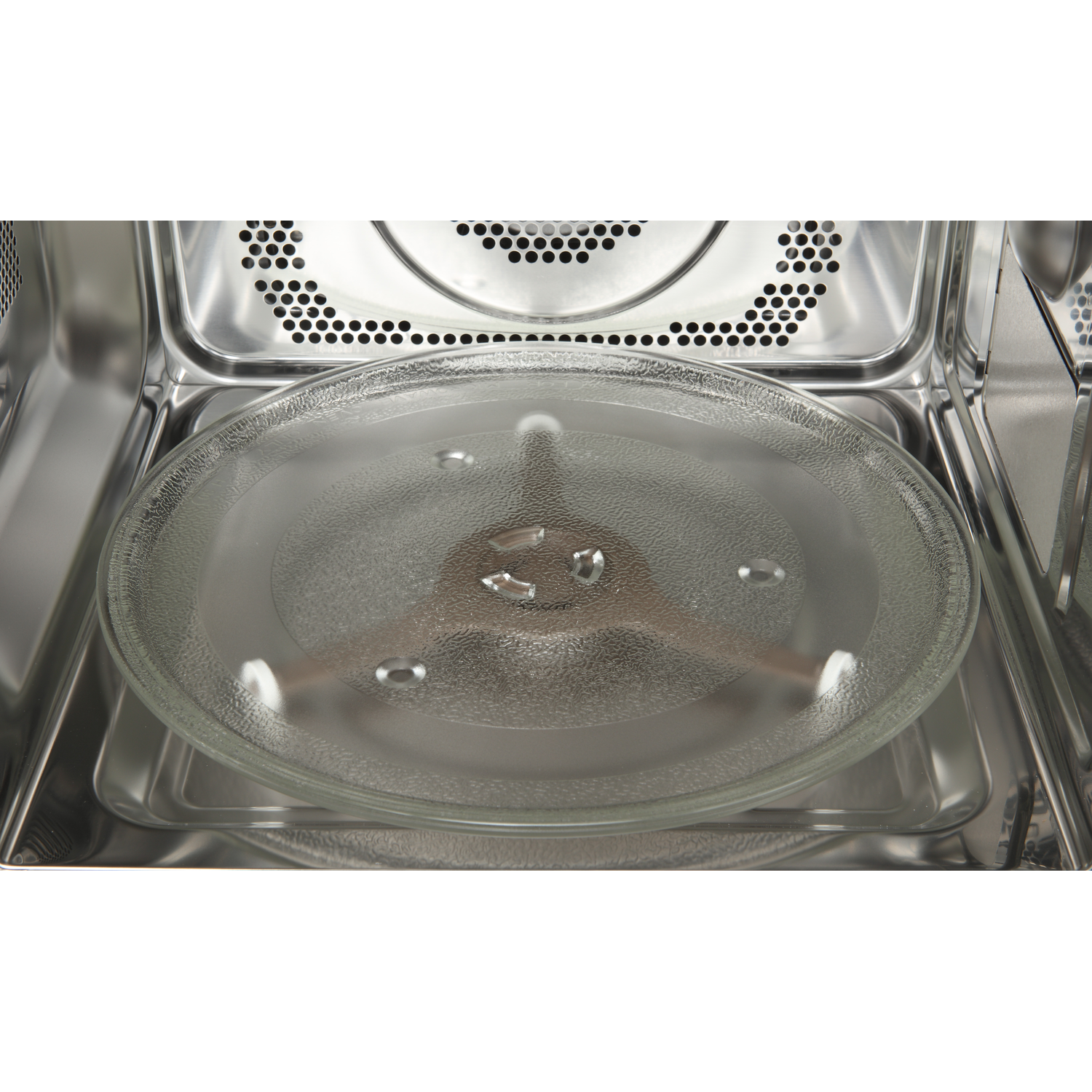 Inside a microwave, a glass plate sits on a rotating base. The interior is stainless steel with ventilation holes at the top.