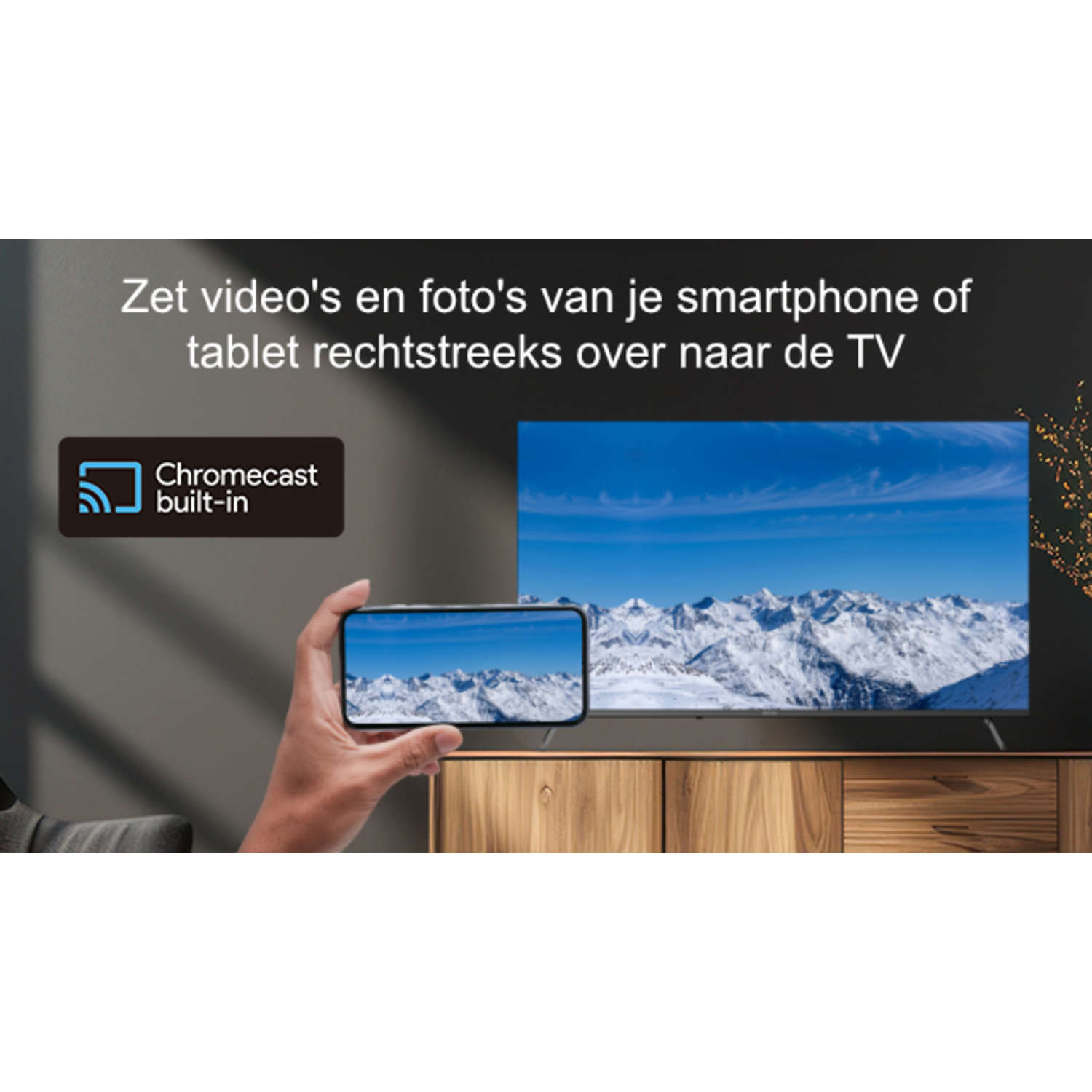 A hand holds a phone showing a mountain view, mirroring a TV screen. The TV sits atop a wooden cabinet. Text: Chromecast built-in.