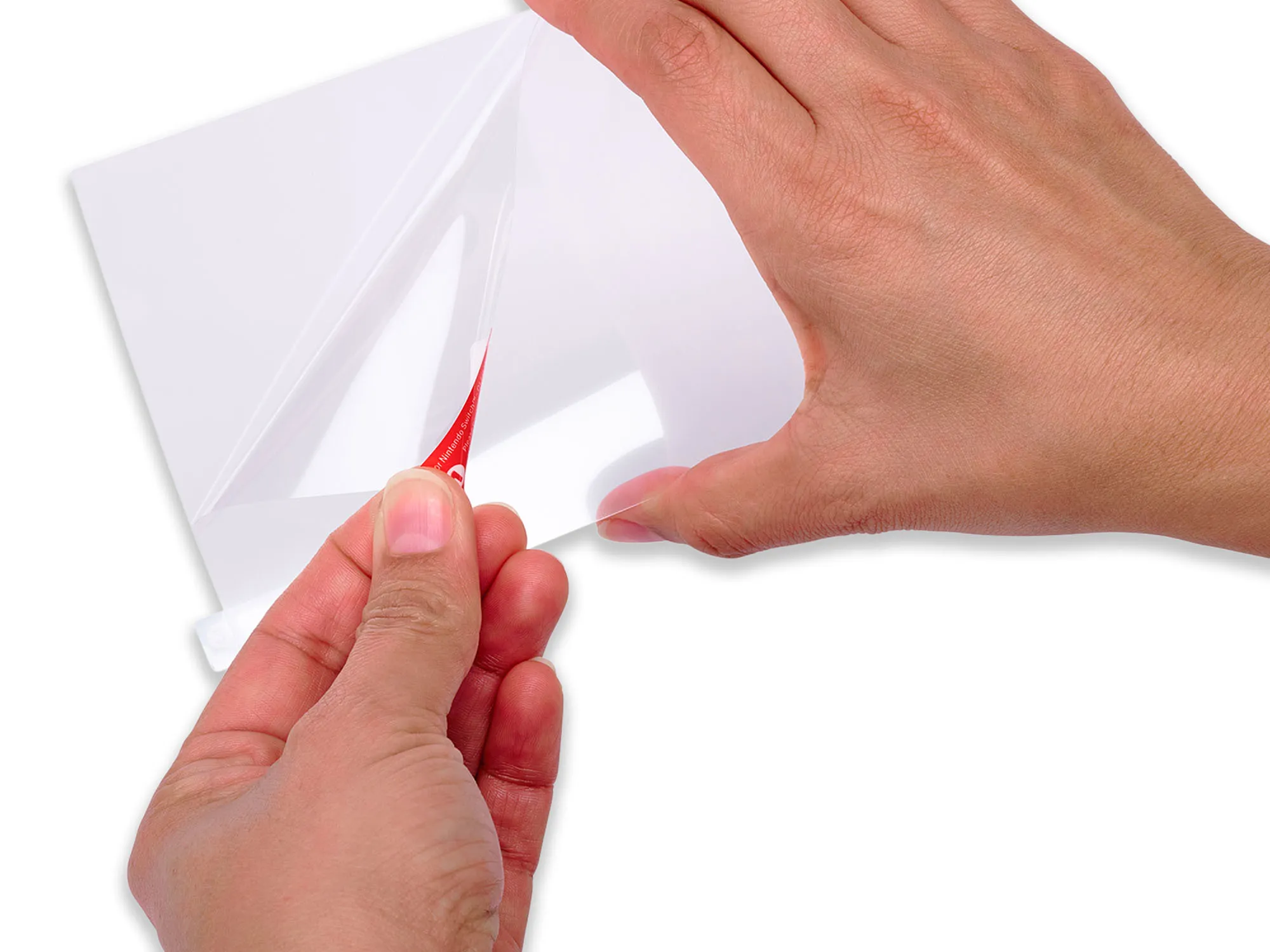 Mani che staccano plastica trasparente da una superficie bianca. È visibile una linguetta rossa. Lo sfondo è bianco.