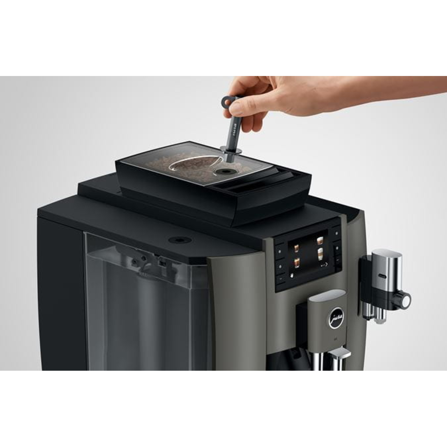 A hand is placing a cleaning tablet into a coffee machine. The machine is black and gray with a digital display and water tank.