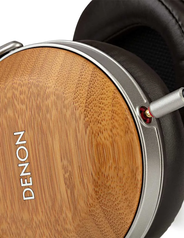 Zbliżenie słuchawek Denon. Muszla uszna ma fakturę drewna ze srebrnym wykończeniem. Widoczna jest czarna skórzana poduszka uszna.