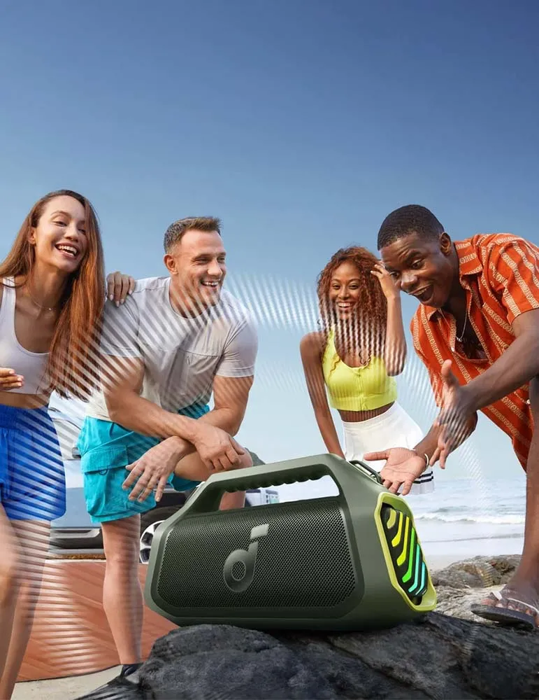 Cztery osoby z przenośnym głośnikiem na skale. Uśmiechają się i śmieją. Tłem jest błękitne niebo i plaża.