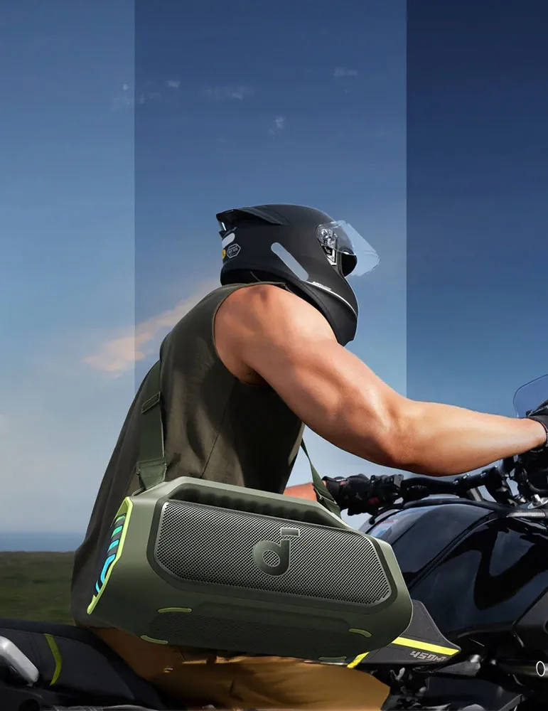 Osoba na motocyklu nosi kask i trzyma głośnik. Tło to błękitne niebo.