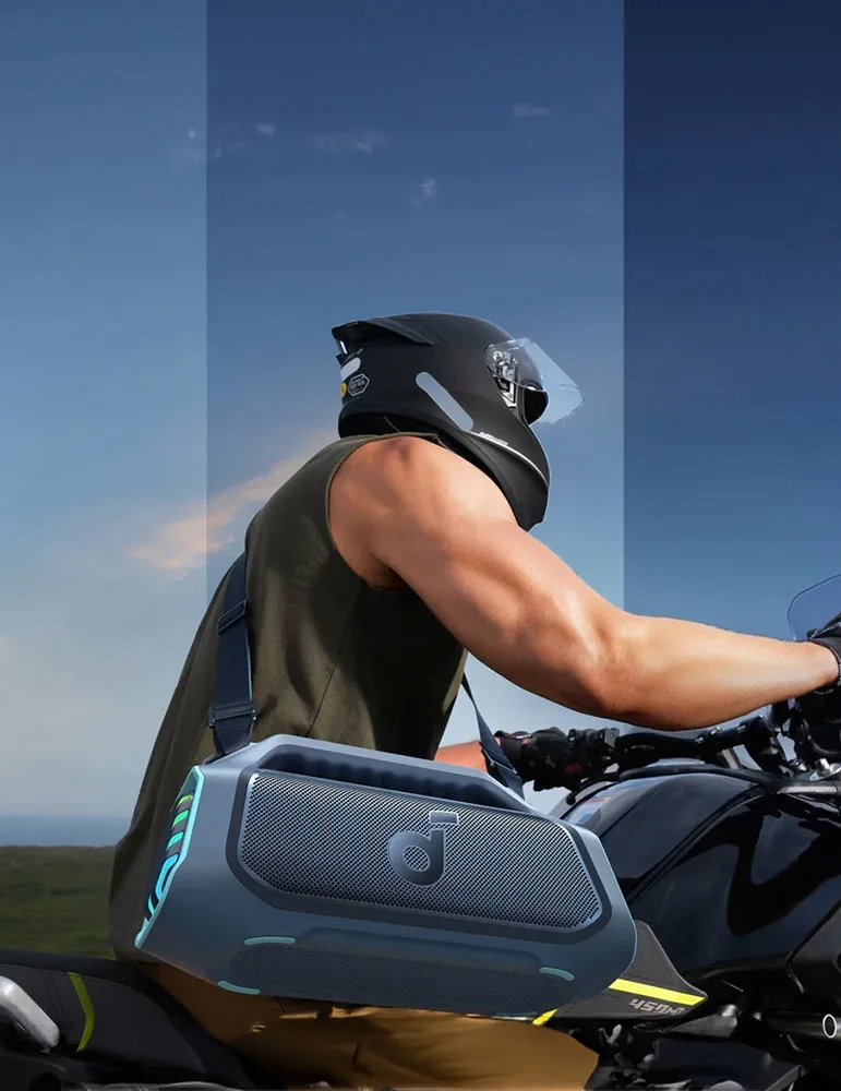 Osoba jedzie motocyklem w kasku, niosąc głośnik. Scena rozgrywa się na zewnątrz z niebieskim niebem.