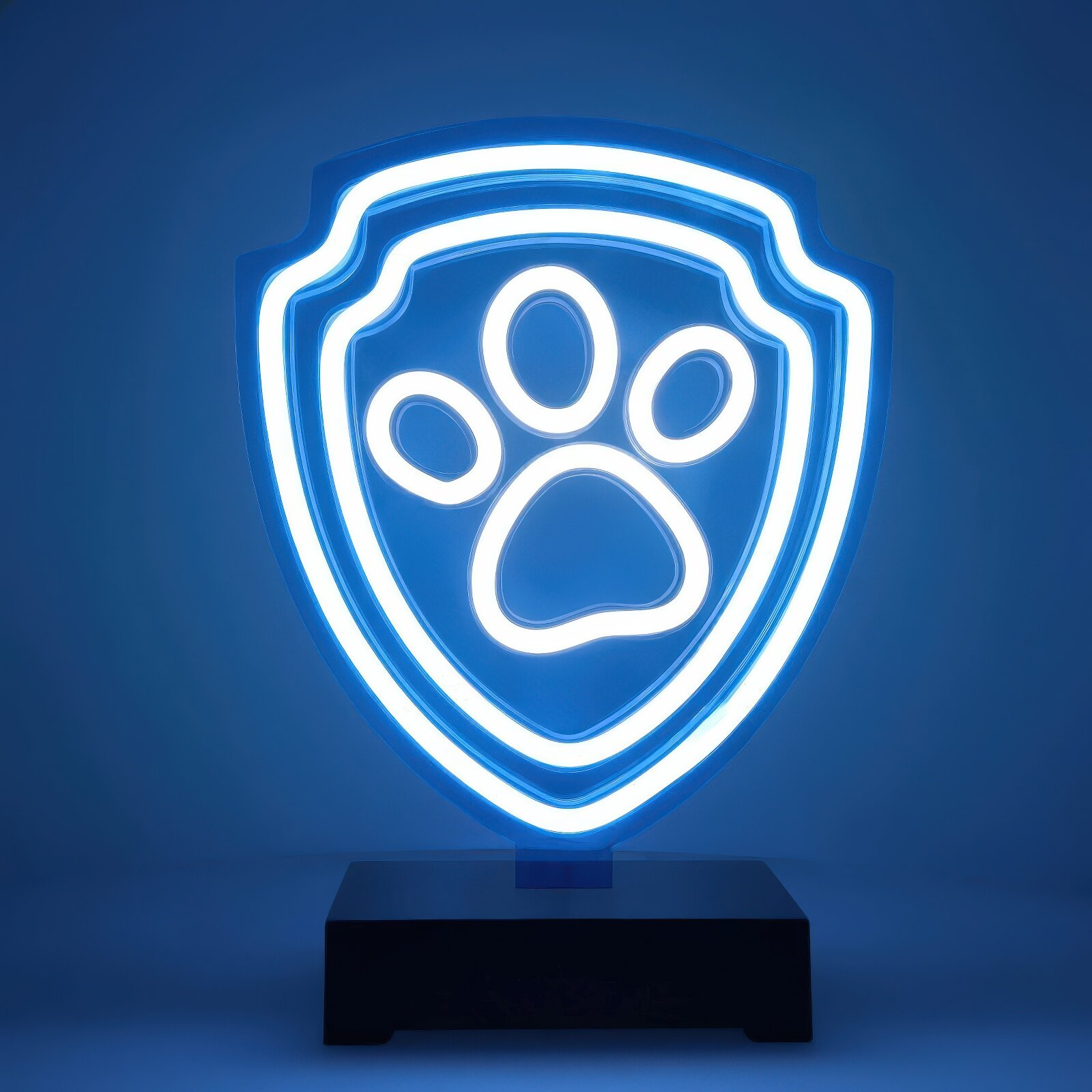 Niebieski neon z logo Paw Patrol, tarcza z odciskiem łapy w środku. Stoi na czarnej podstawie.