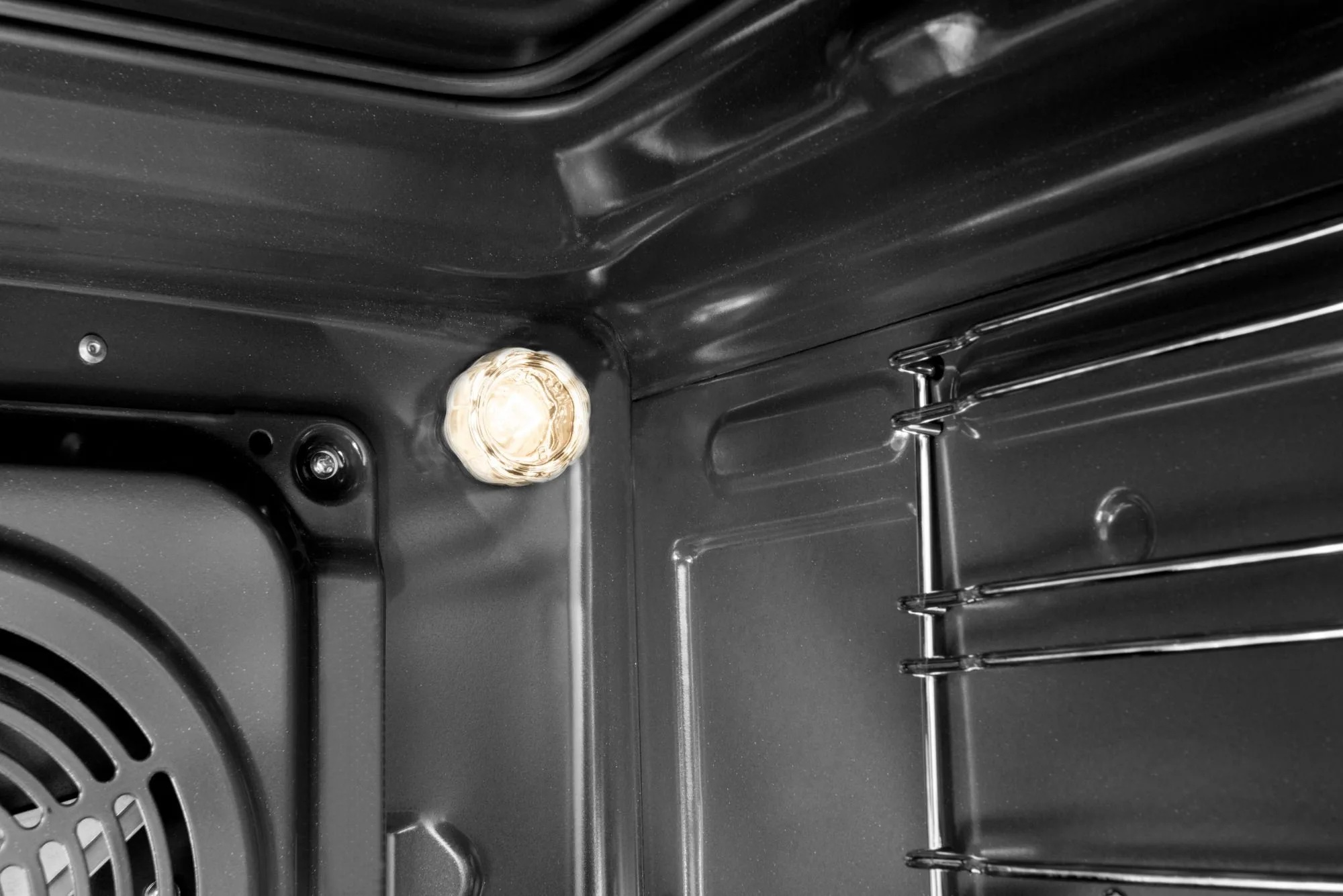 Wewnątrz ciemnego piekarnika jasne światło oświetla wnętrze. Kratki piekarnika widoczne po prawej stronie. Wnętrze piekarnika jest czarne.