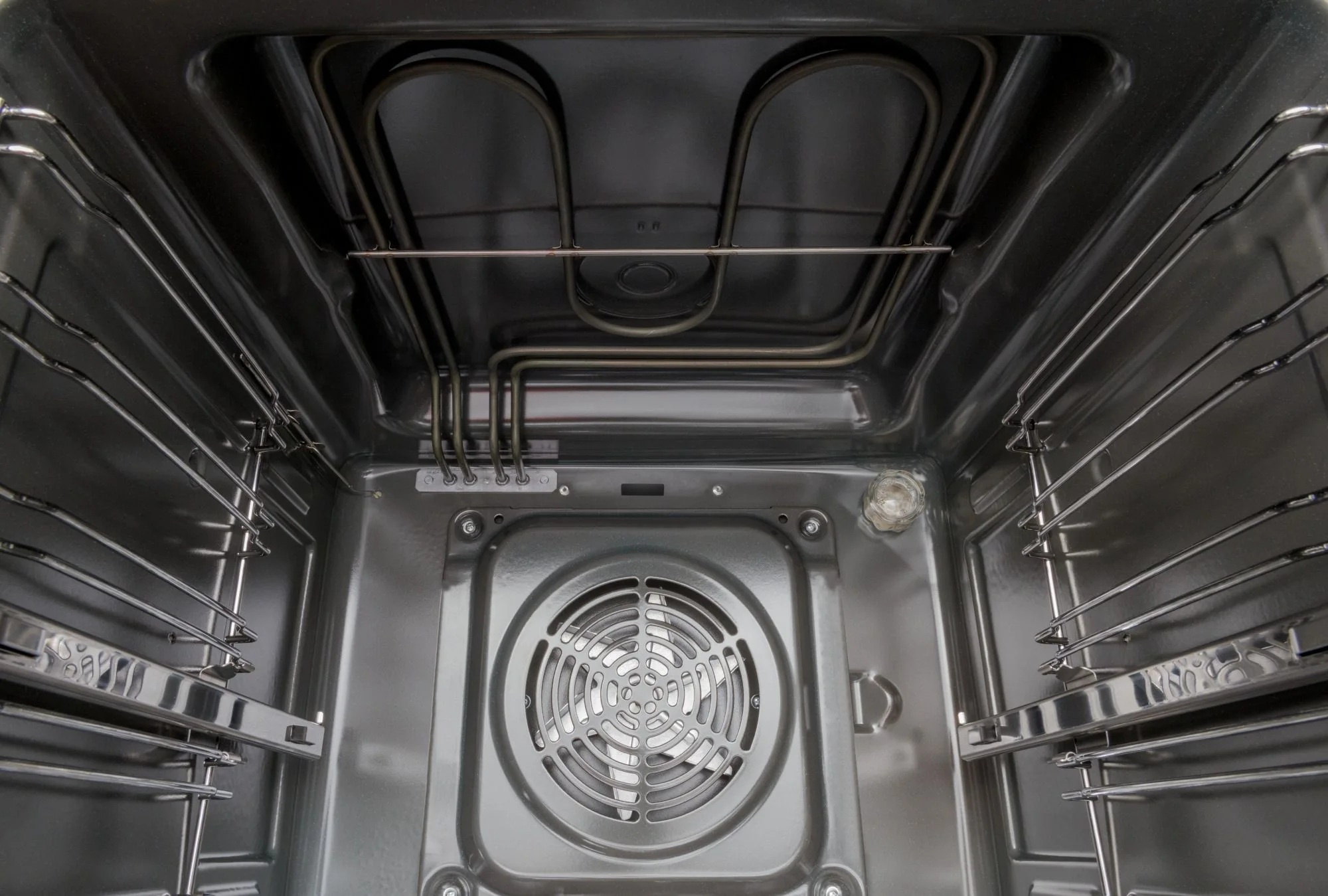 Widok wewnątrz piekarnika. Widoczne elementy grzejne i ruszty. Wentylator znajduje się na środku. Wnętrze jest metaliczne.