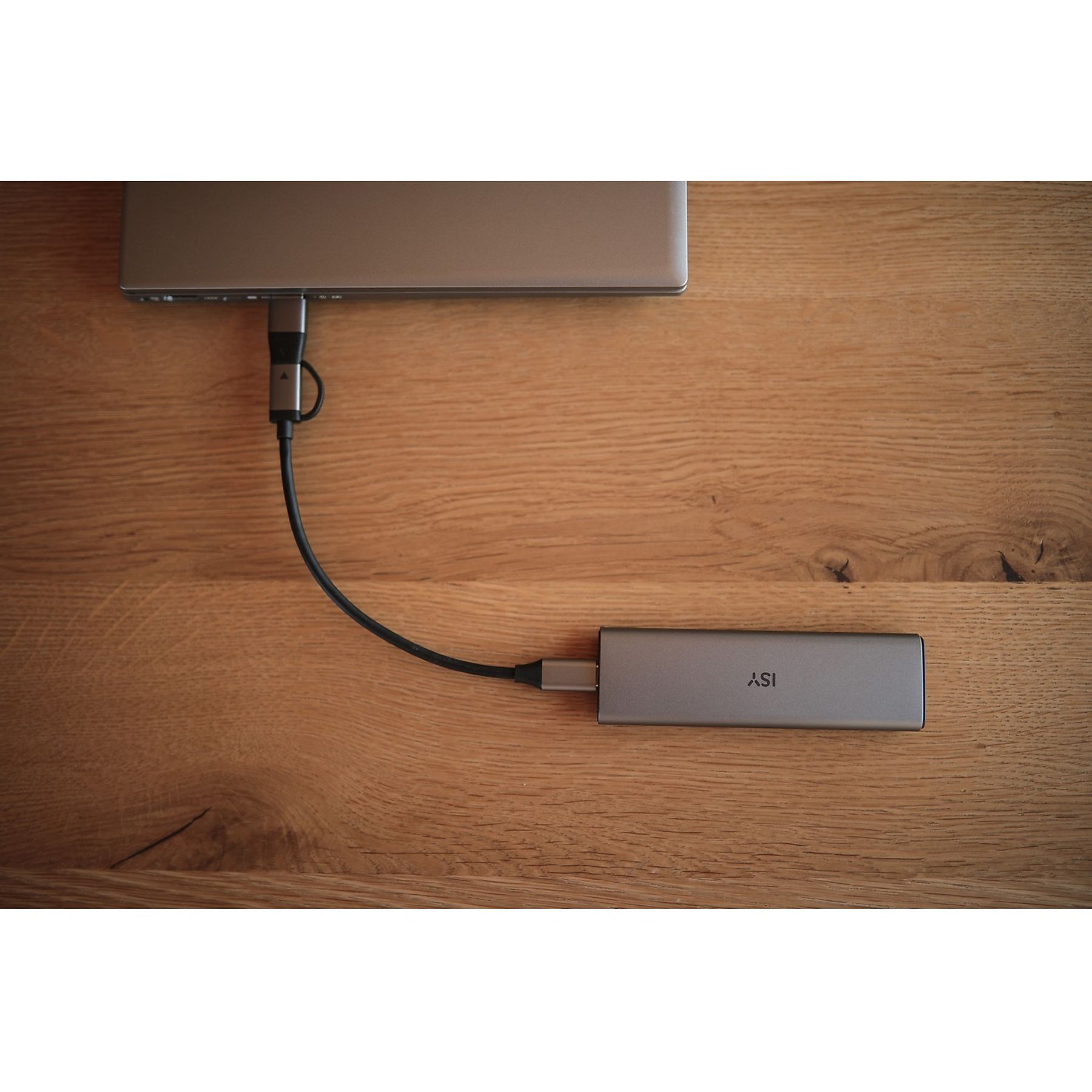 Laptop podłączony do szarego huba USB czarnym kablem, na drewnianej powierzchni. Hub ma etykietę 'ISY'.