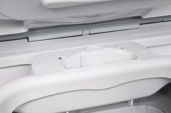 Zbliżenie na białe wnętrze lodówki. Widoczny uchwyt i kilka białych plastikowych elementów, tworzących czystą, nowoczesną estetykę.