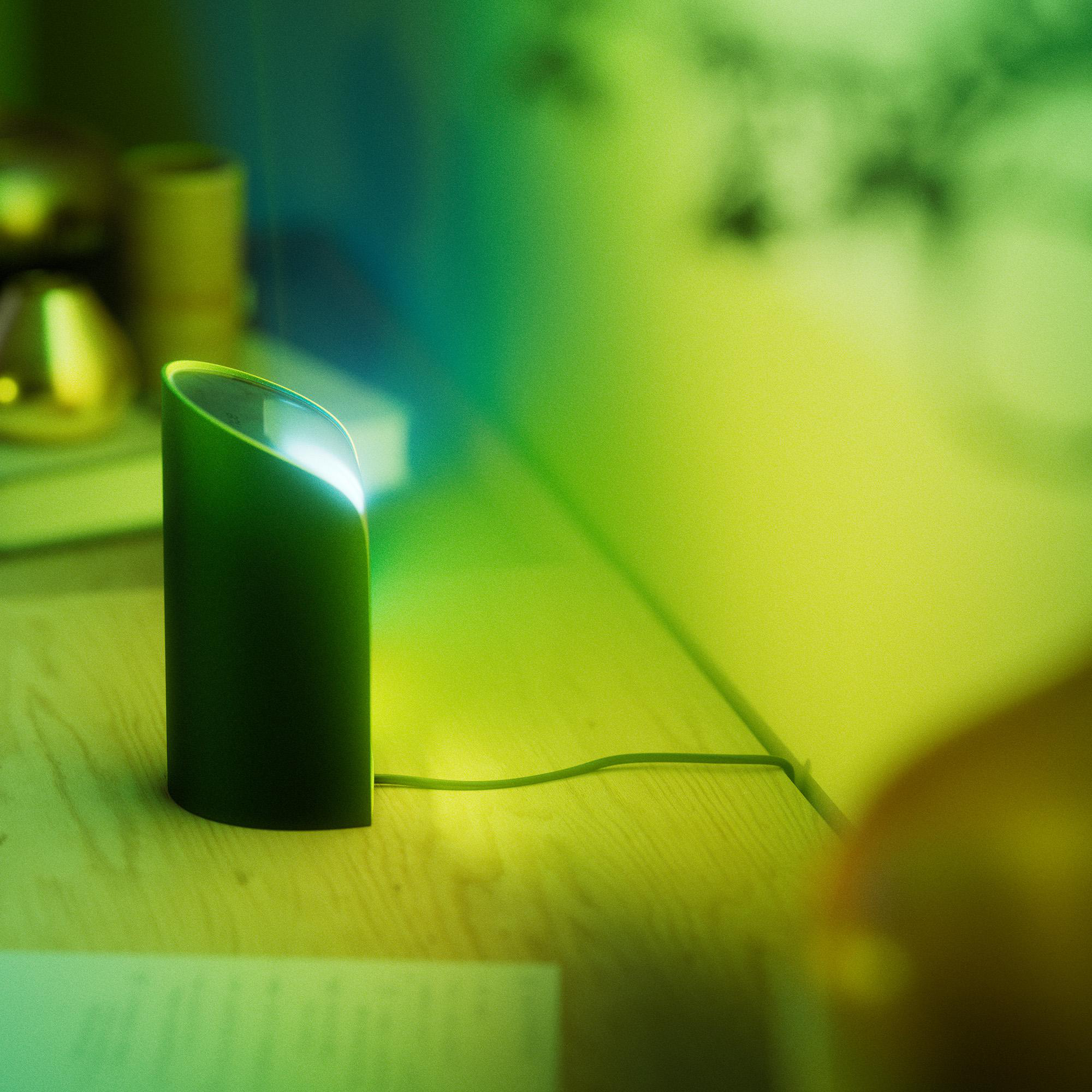 Grüne Lampe auf Holzoberfläche. Helles Licht, das von oben austritt. Andere Objekte im Hintergrund sind unscharf.