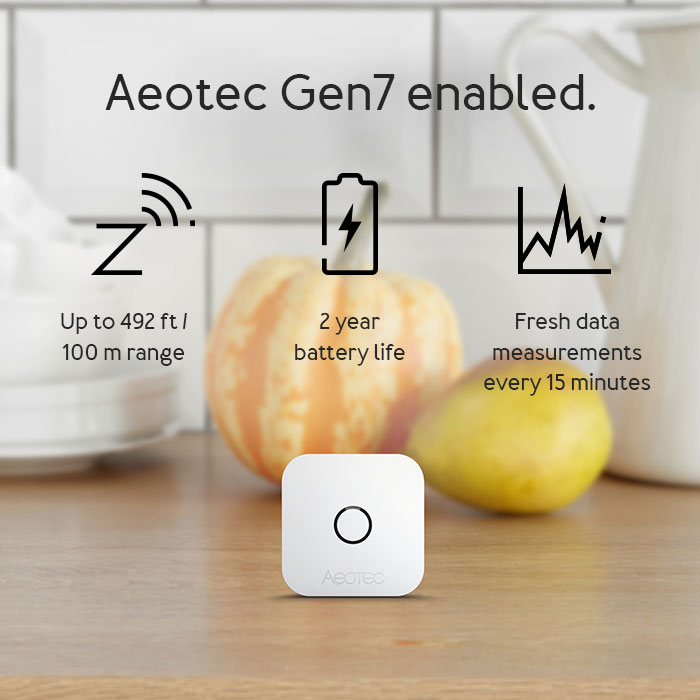 Fehér Aeotec eszköz fekete körrel, gyümölccsel és hatótávolság, akkumulátor-élettartam és adatméretek ikonokkal, konyhai háttérrel.