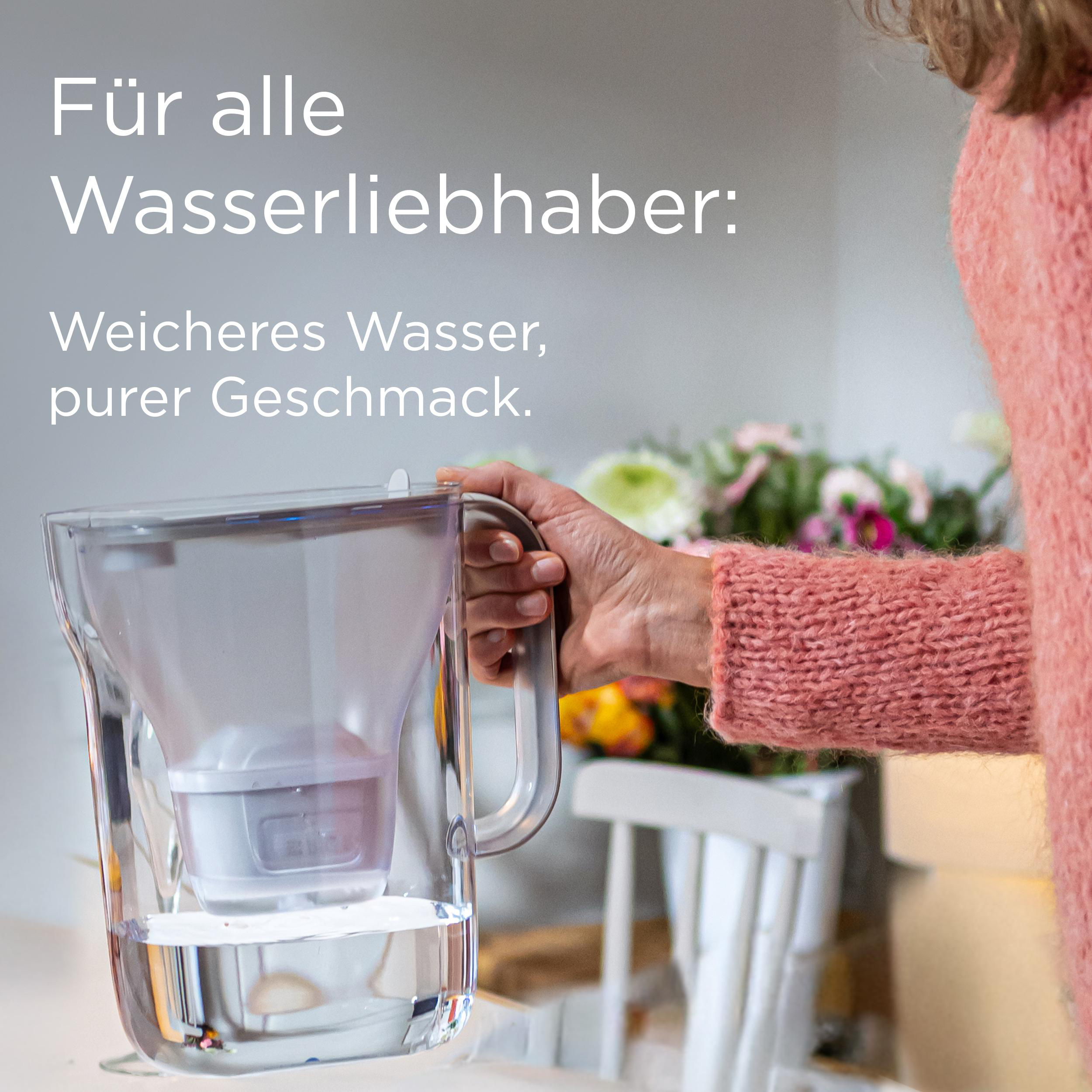 Eine Person hält einen Wasserfilter, mit deutschem Text. Ein rosa Pullover ist im Bild, zusammen mit Blumen und einem Stuhl.