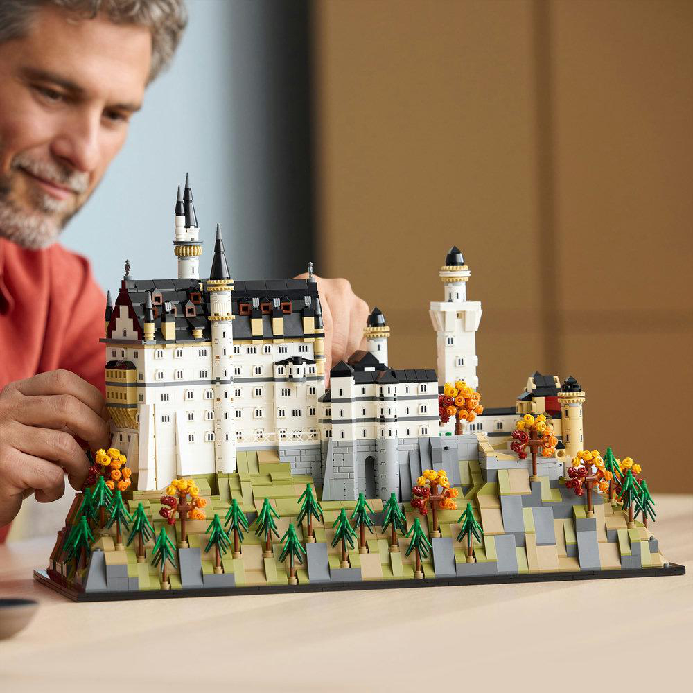 Ein Mann baut ein Lego-Schloss. Das Schloss ist weiß, schwarz und grau, mit Bäumen und Büschen auf einer grünen und grauen Basis.
