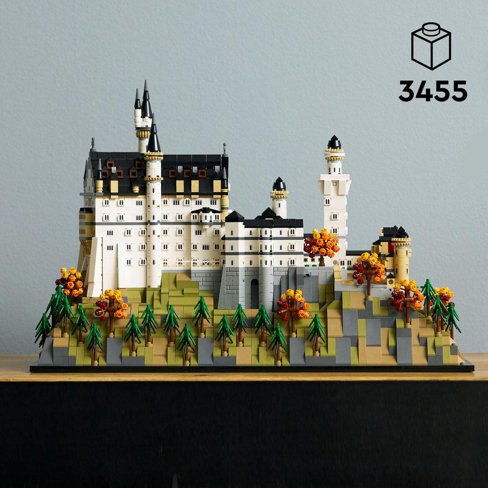 LEGO-Modell eines weißen Schlosses mit schwarzen Dächern und Türmen, auf einem Hügel mit Bäumen und Laub, auf einer Holzoberfläche.