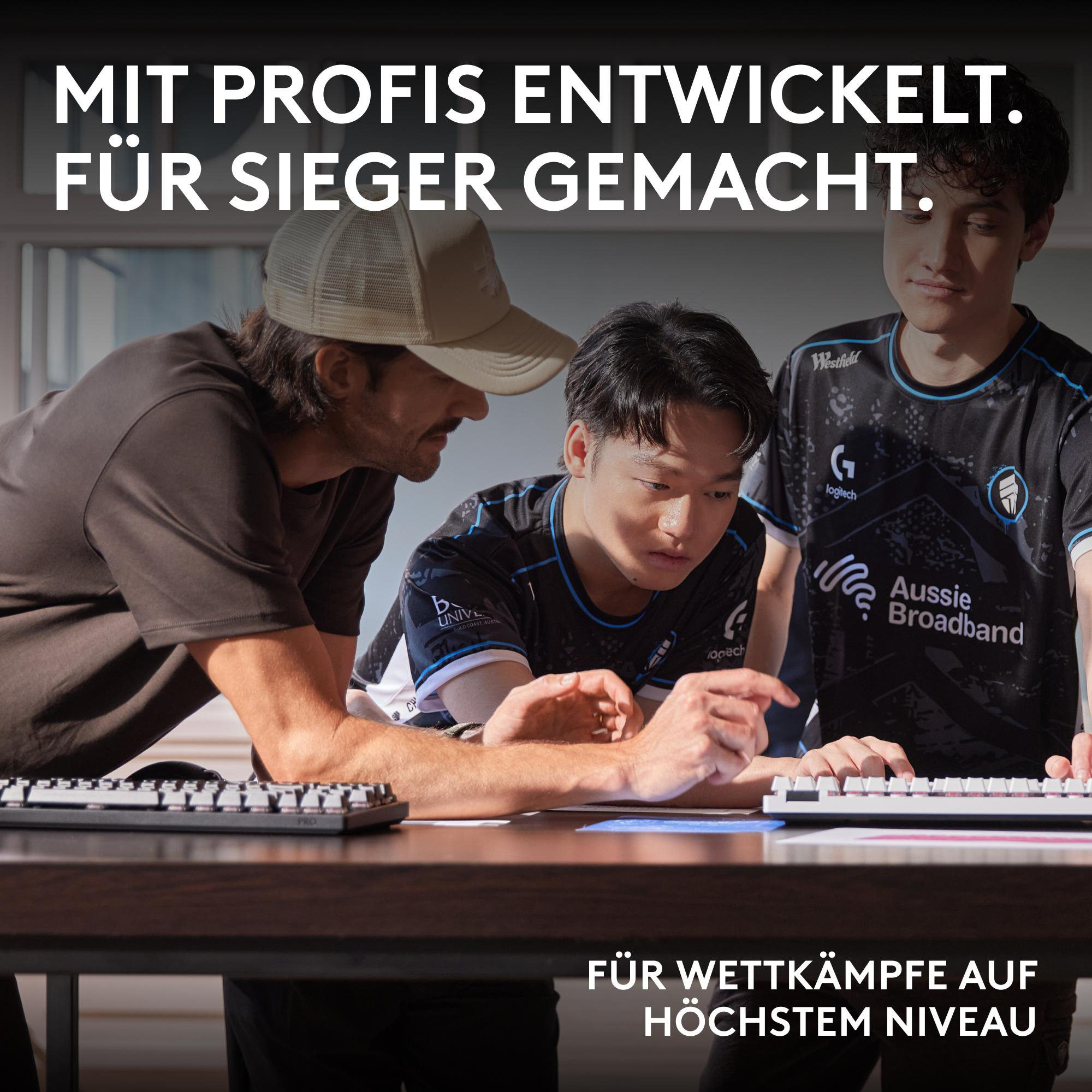 Drei Männer betrachten eine Tastatur. Text sagt: 'Entwickelt mit Profis. Gemacht für Sieger. Für Wettkämpfe auf höchstem Niveau.'