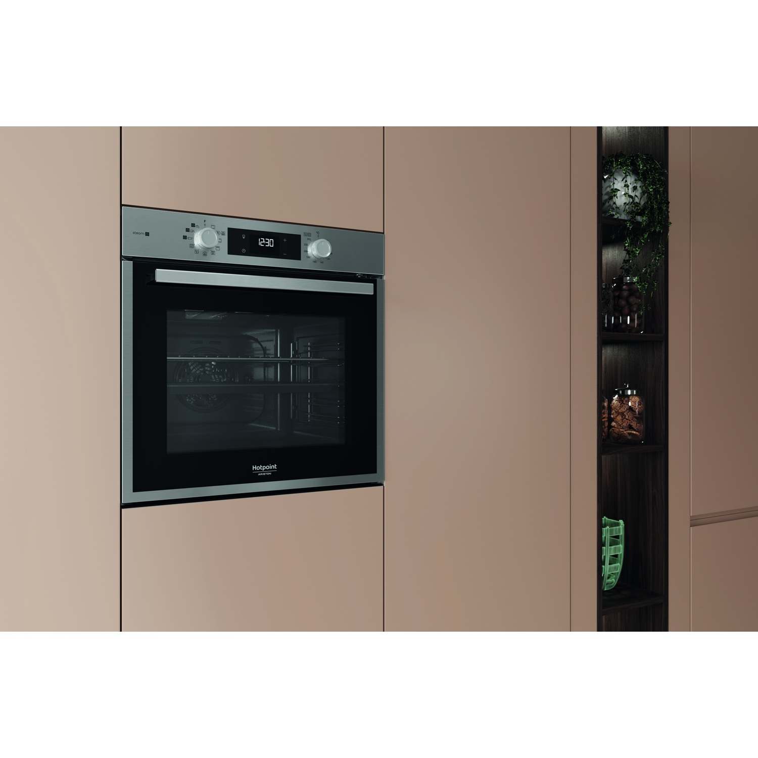 Un forno Hotpoint a incasso con orologio digitale. Il forno è integrato in un mobile da cucina. A destra c'è una mensola con piante e barattoli.