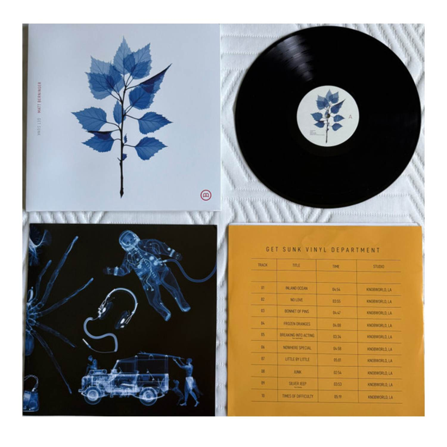 Une pochette d'album avec des feuilles bleues, un disque vinyle noir et des images radiographiques d'une araignée, d'un astronaute et d'une jeep.