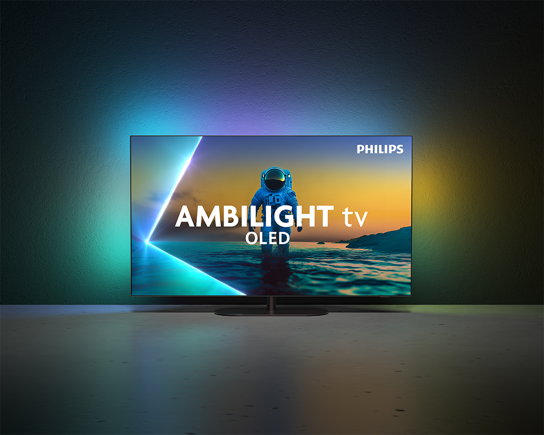 Egy Philips OLED TV egy űrhajóst jelenít meg egy strandon az 'AMBILIGHT tv OLED' felirattal. A TV egy sötét felületen van.
