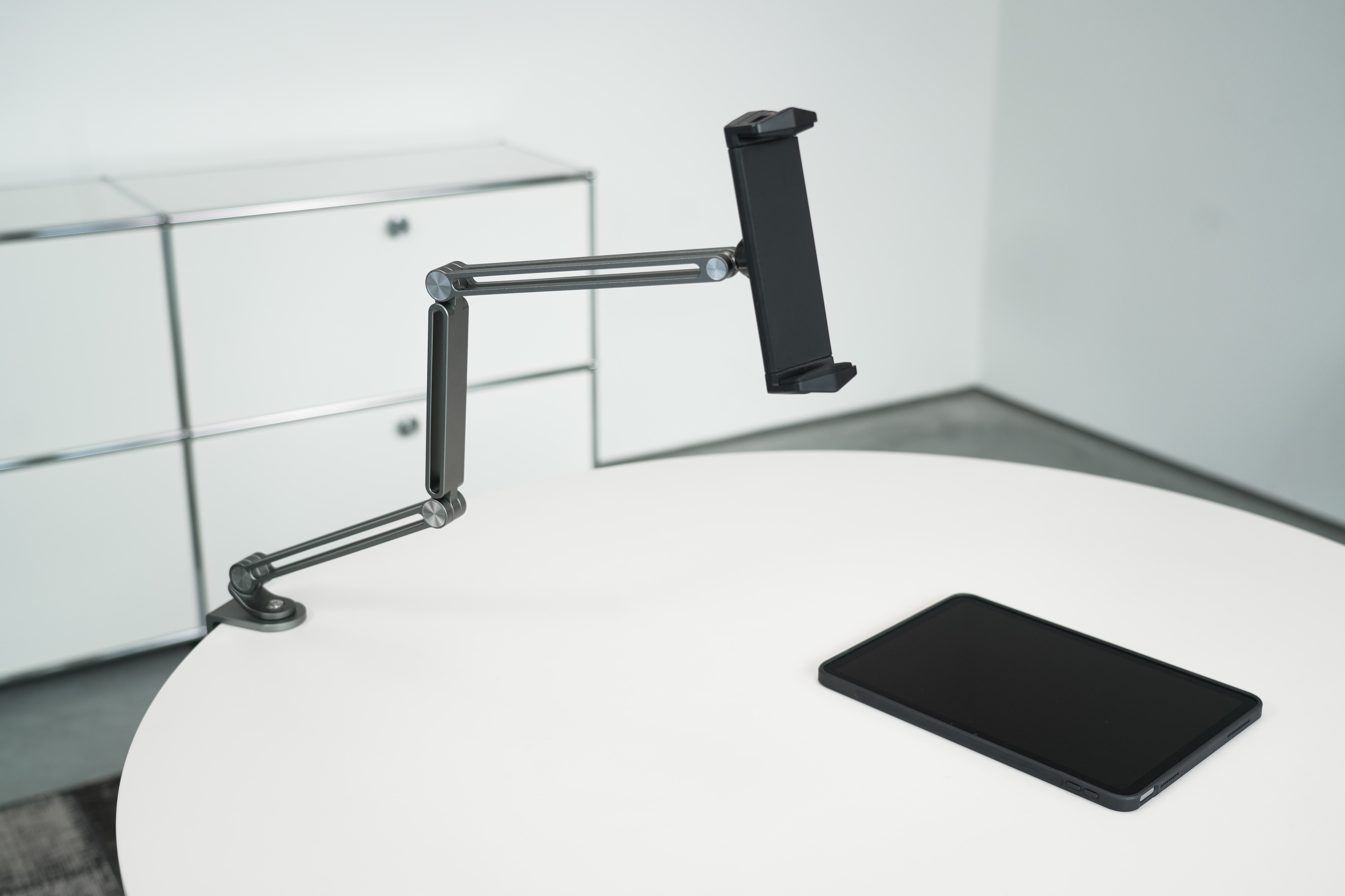 Ein schwarzes Tablet auf einem weißen Tisch, mit einem schwarzen Tablethalter. Weißer Schrank im Hintergrund.