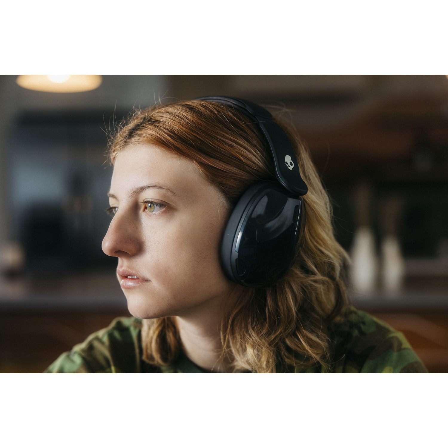 Une jeune femme aux cheveux roux porte un casque noir et regarde vers la gauche. Elle a les yeux verts et porte une chemise camouflage.