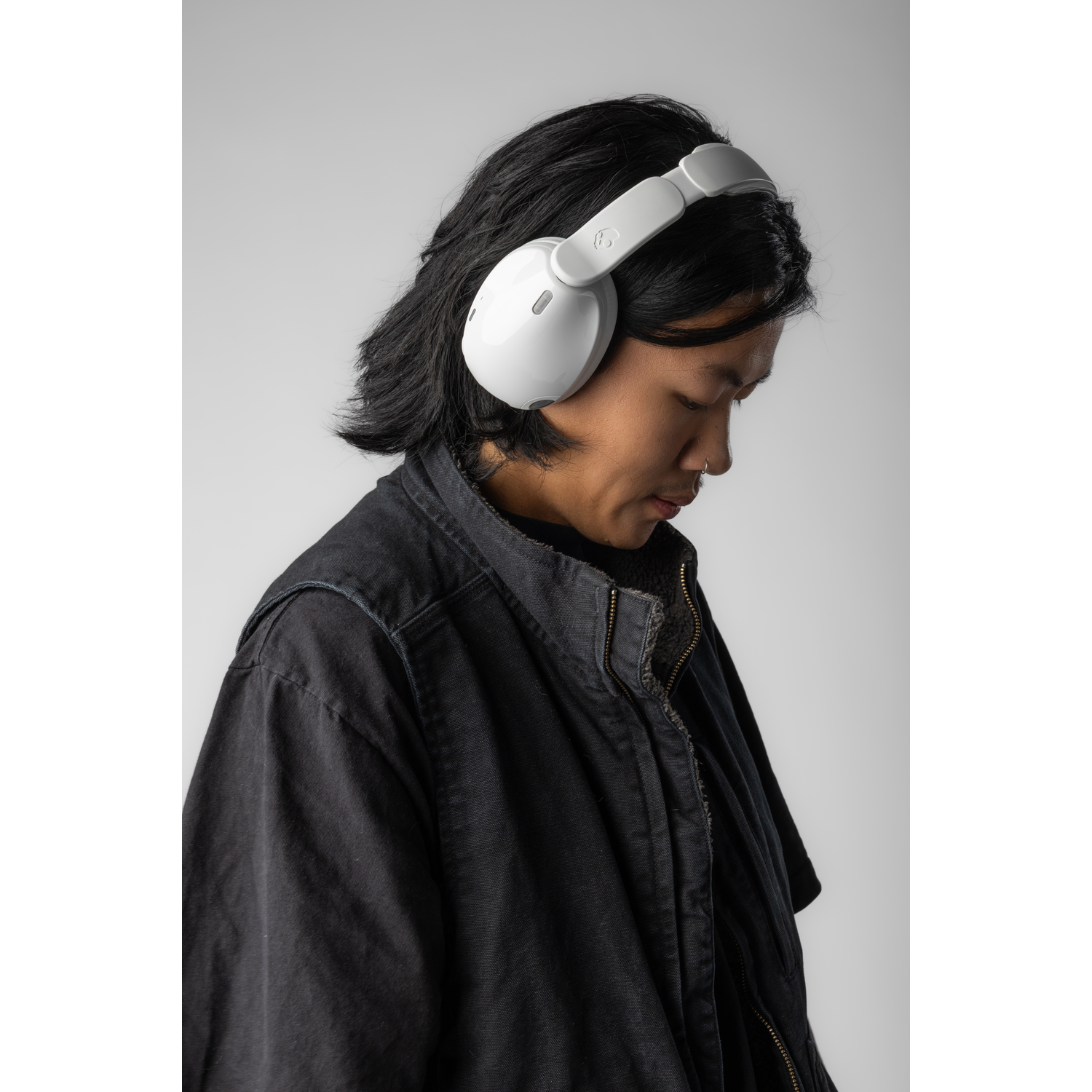 Une personne portant un casque blanc et une veste noire. La personne regarde vers le bas. Le fond est gris clair.