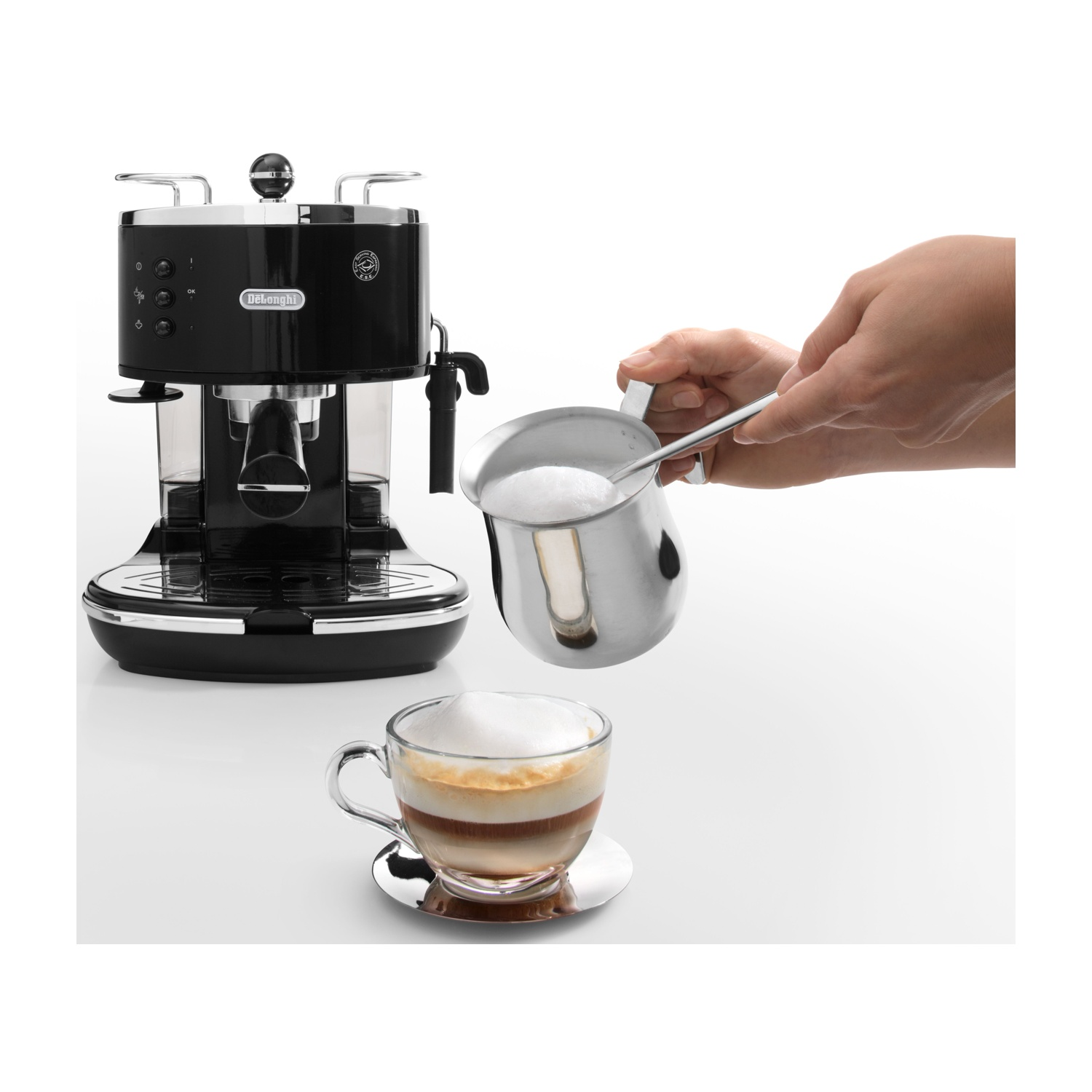 Una persona versa la schiuma di latte in un cappuccino. Sono presenti anche una macchina per caffè espresso nera e una tazza di vetro con un piattino d'argento.