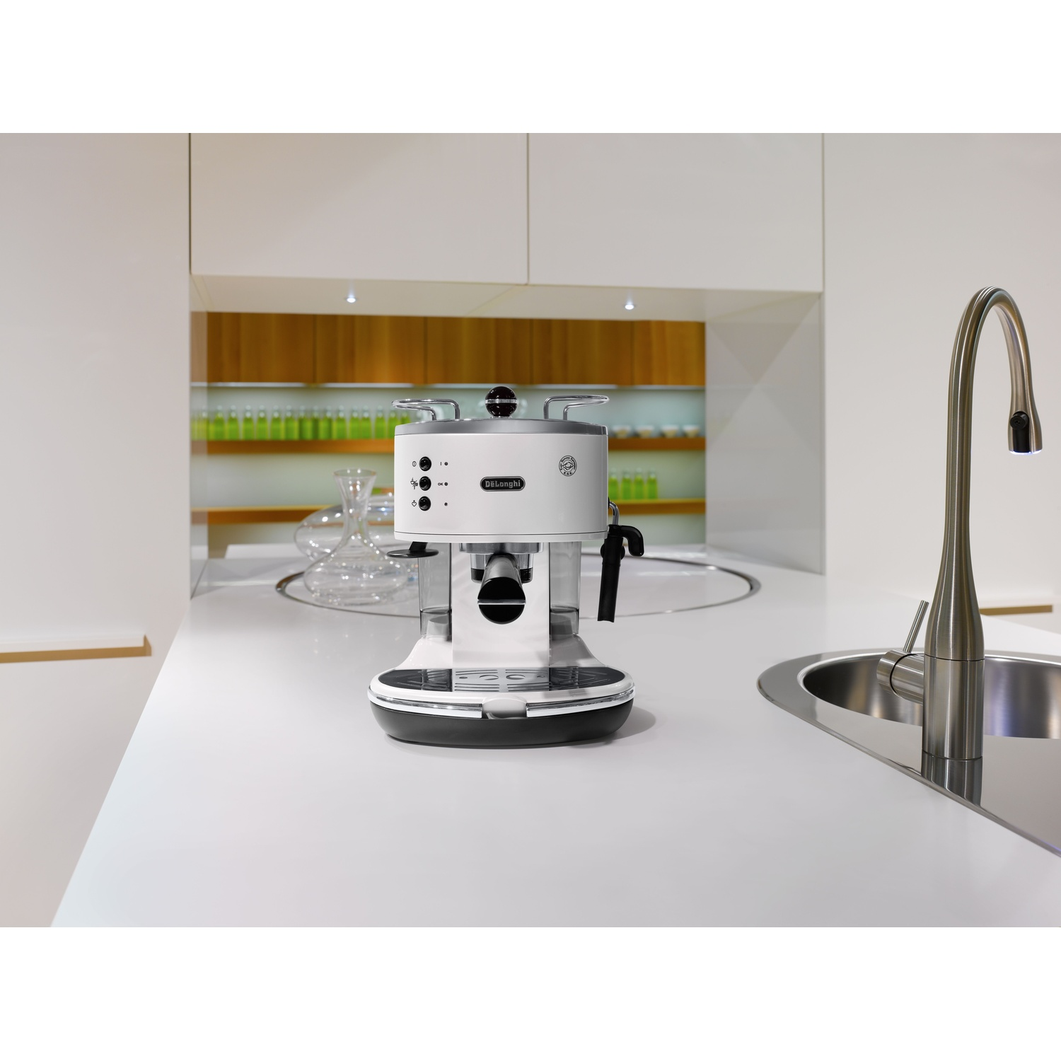 Una macchina per caffè espresso bianca è su un ripiano bianco. A destra ci sono un rubinetto e un lavandino in acciaio inossidabile. Armadi bianchi sullo sfondo.