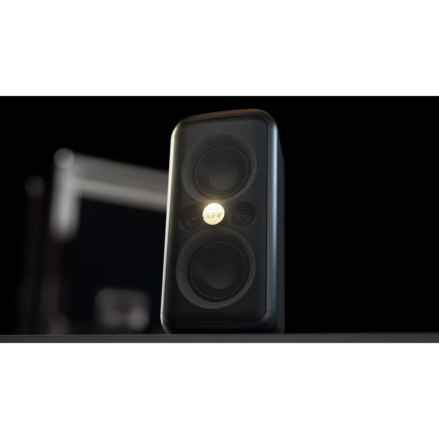 A black speaker with a mesh front and a golden logo sits on a shelf against a dark background. Another object is blurred.