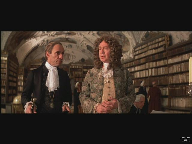 Zwei Männer in historischer Kleidung unterhalten sich in einer Bibliothek. Bücherregale säumen die Wände.