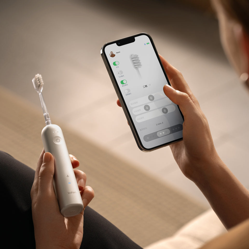 Egy személy egy fehér elektromos fogkefét és egy beállításokat mutató telefont tart. A telefon egy fogkefe-diagramot és vezérlési lehetőségeket mutat.