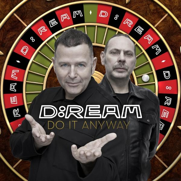 Zwei Männer stehen vor einem Roulette-Rad. Die Band D:Ream ist davor. Eine weiße Kugel liegt auf dem Rad.