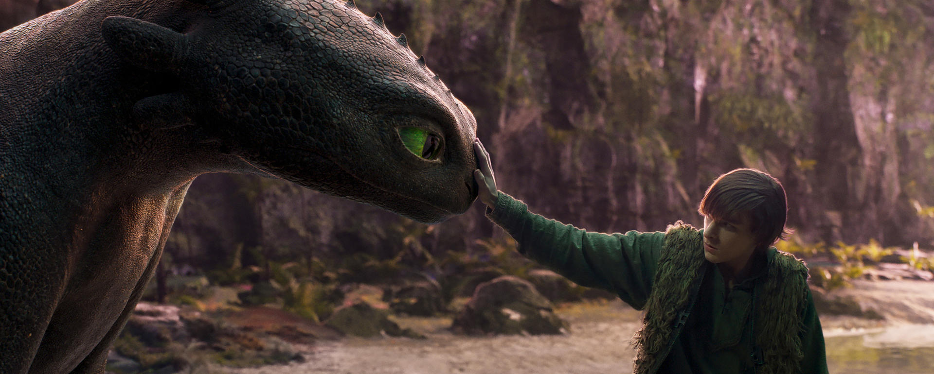 Ein junger Mann berührt den Kopf eines Drachen. Der Drache ist schwarz mit grünen Augen. Der Mann trägt grüne Kleidung.