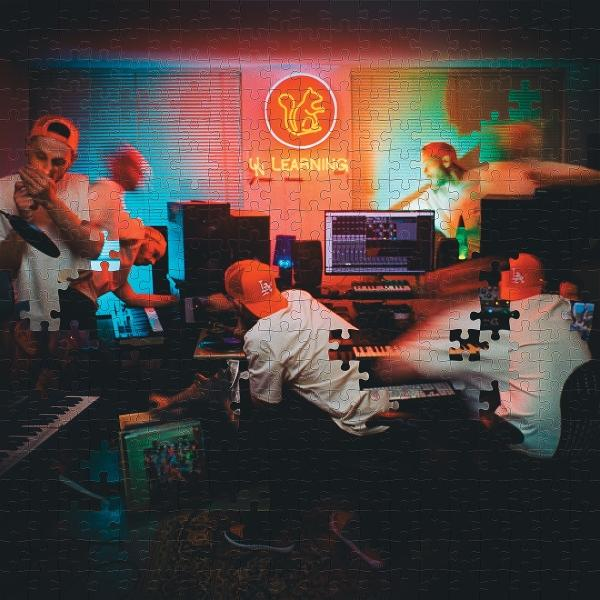 Verschwommene Figuren in einem Studio. Musiker mit orangefarbenen Kappen und weißen Hemden arbeiten an Ausrüstung unter einem Neonschild.