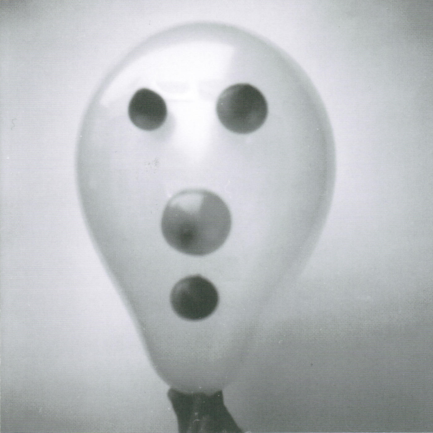 Ein Graustufenbild eines Ballons mit drei kreisförmigen dunklen Flecken, die Augen und Mund ähneln, auf hellem Hintergrund.