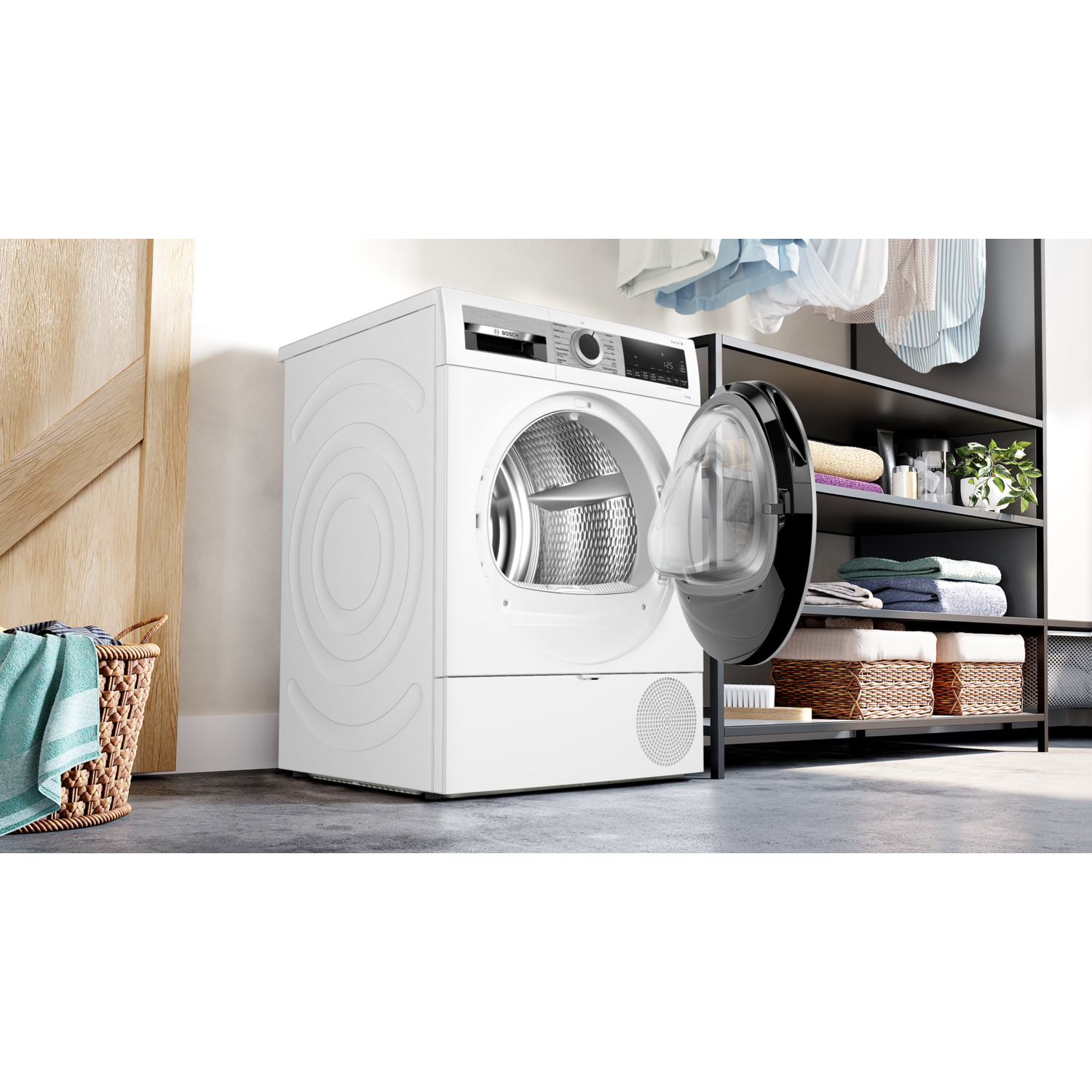 A white dryer with an open door. A basket with a towel is on the left, shelves with folded towels are in the back.