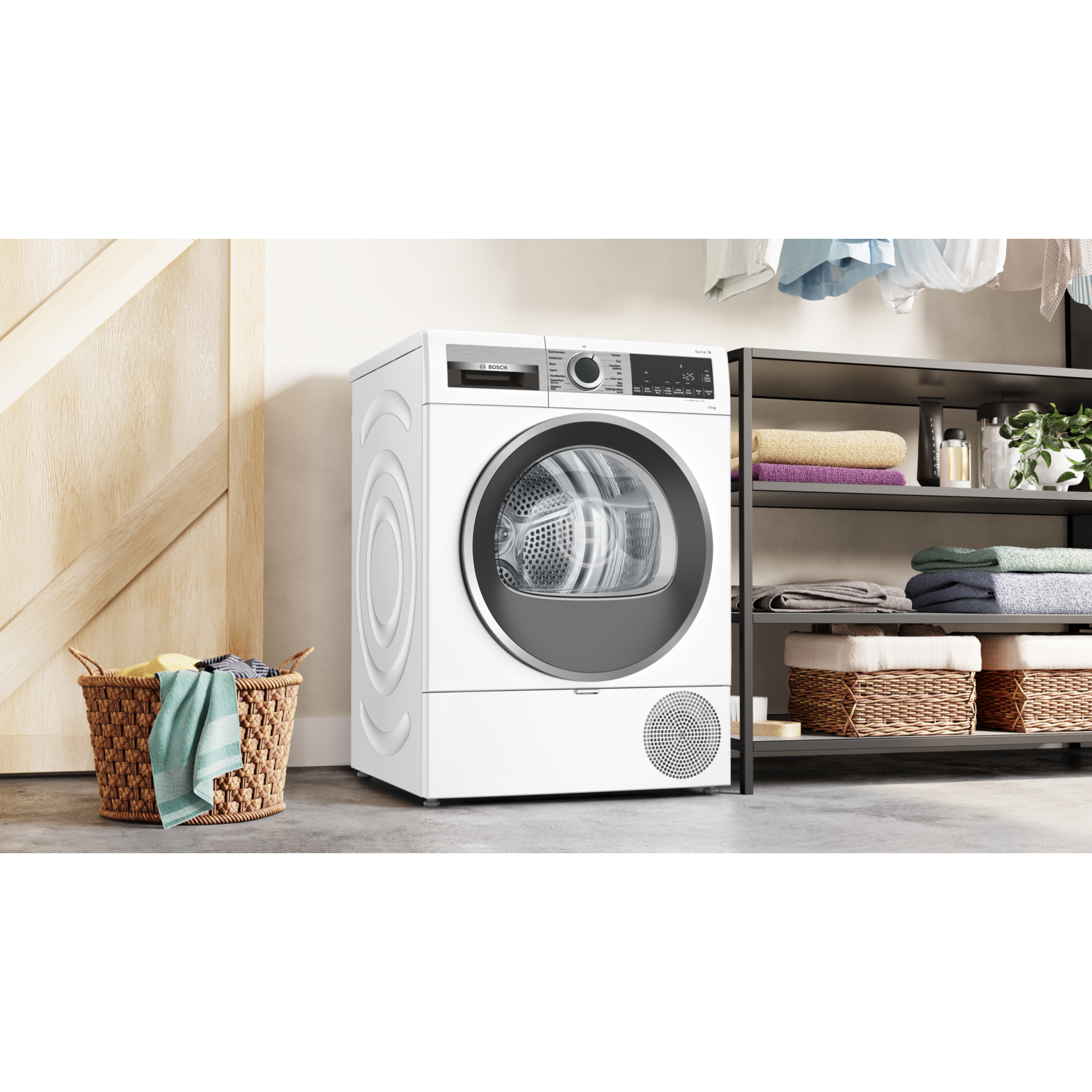 A white dryer is in a laundry room. A basket of laundry is to the left. Shelves with towels are on the right.