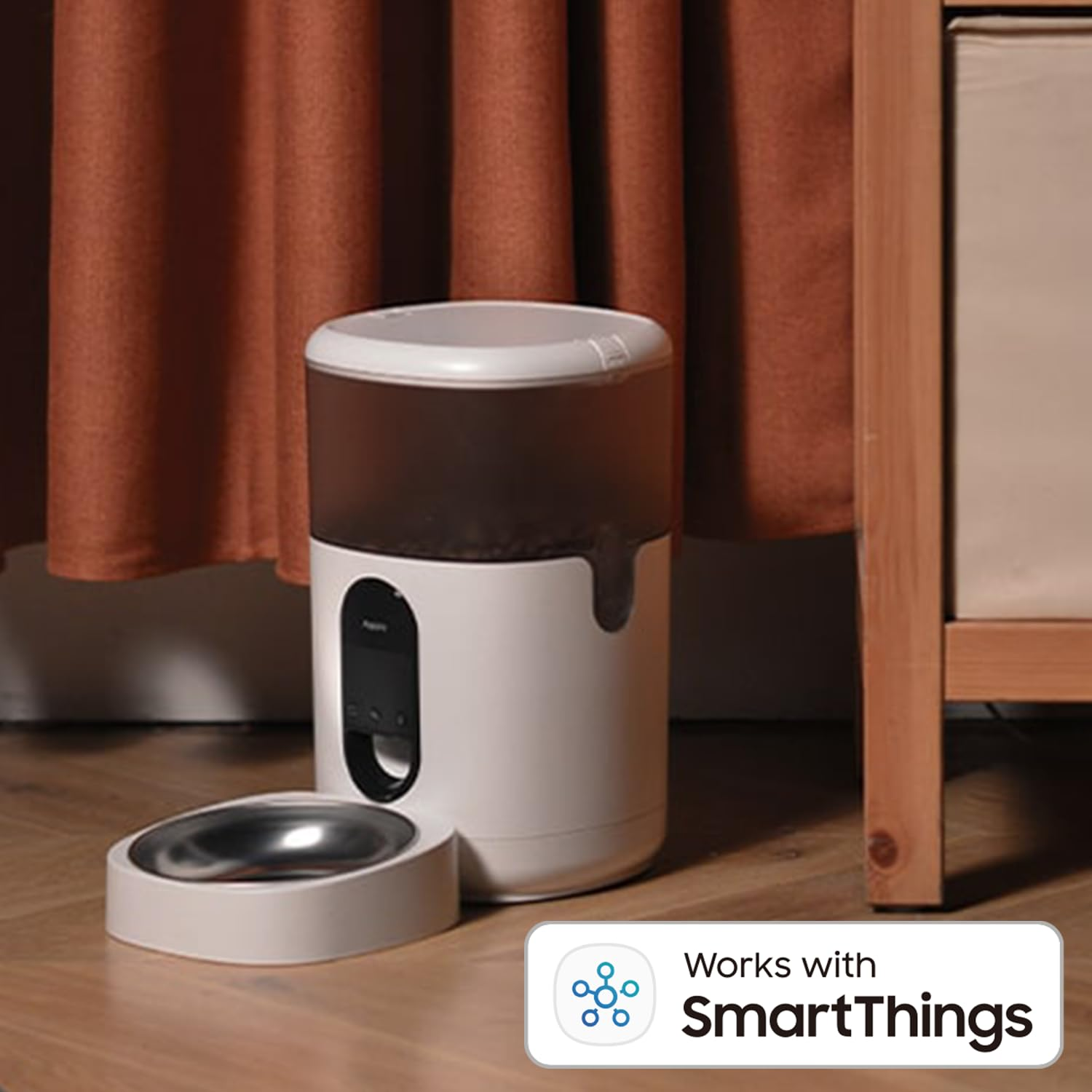 Fehér és barna kisállat-etető rozsdamentes acél tálkával. A háttérben barna függöny látható. Egy 'Works with SmartThings' logó látható.