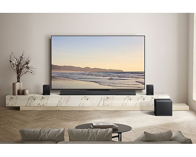 Nappali nagy TV-vel, hangrendszer hangszórókkal és mélynyomóval. Elöl kanapé és dohányzóasztal.