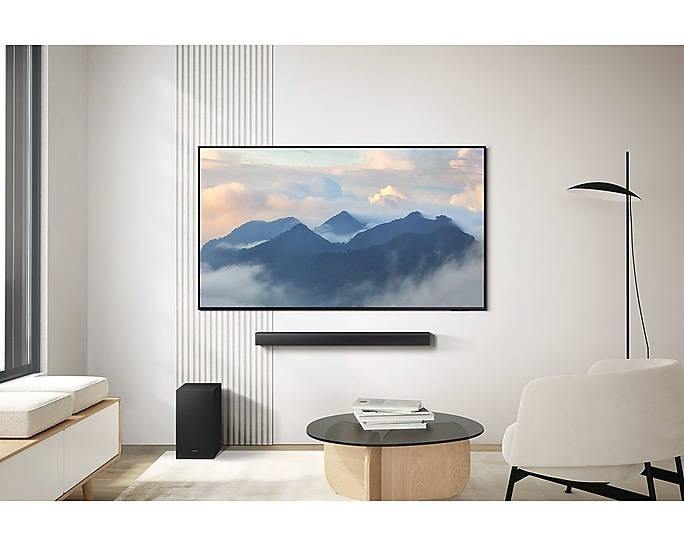 Nappali hegyeket mutató TV-vel. Hangprojektor, mélynyomó, dohányzóasztal, lámpa és szék is látható.
