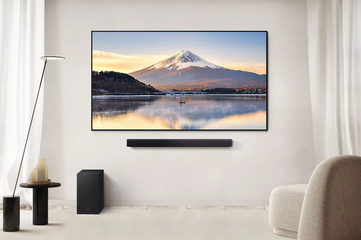 Egy TV hegyi jelenetet mutat. Hangprojektor és mélynyomó található alatta. Egy lámpa és egy szék van az oldalakon.