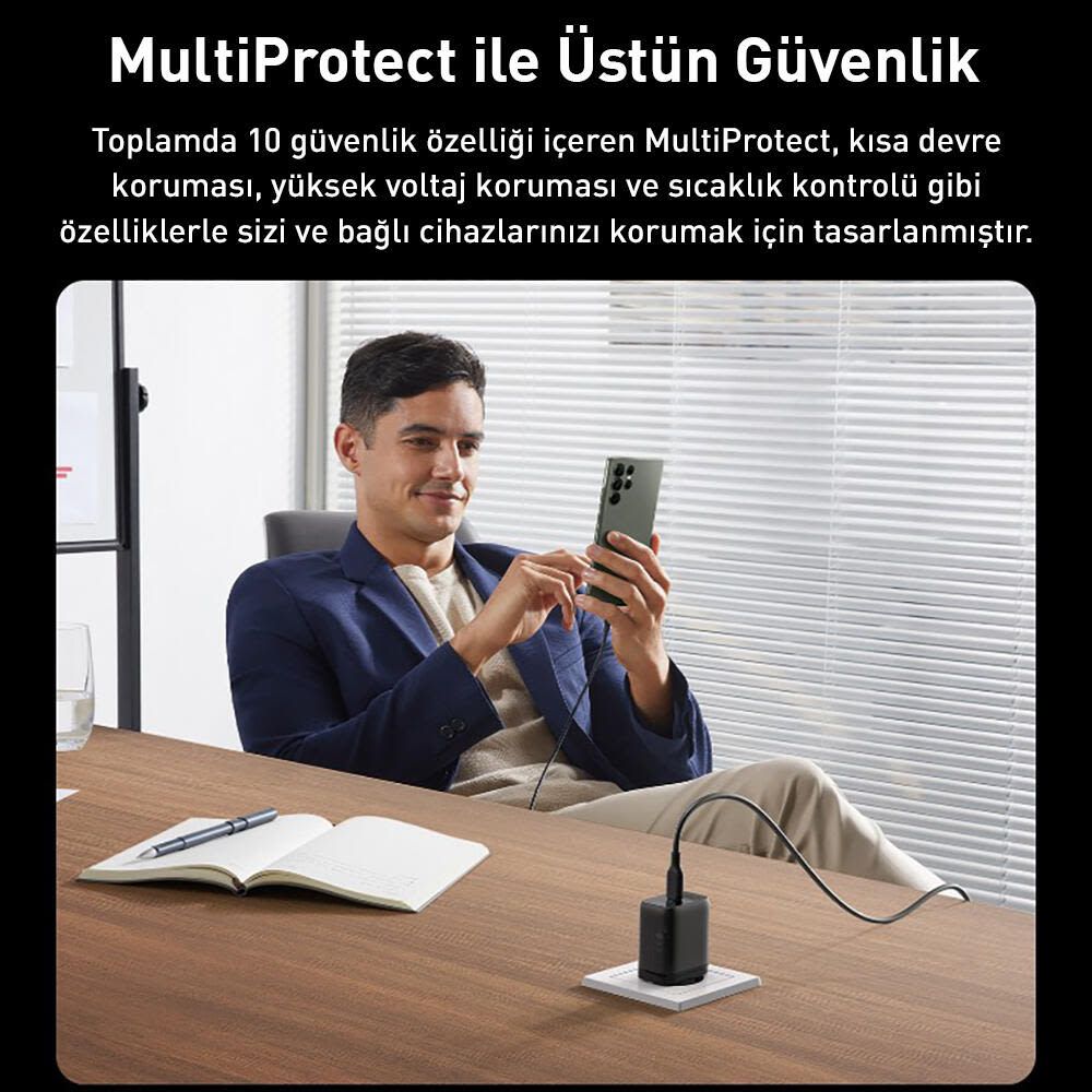 Ceketli bir adam, bir masadaki şarj cihazına bağlı telefonuna bakıyor. Masada bir not defteri ve kalem de var.