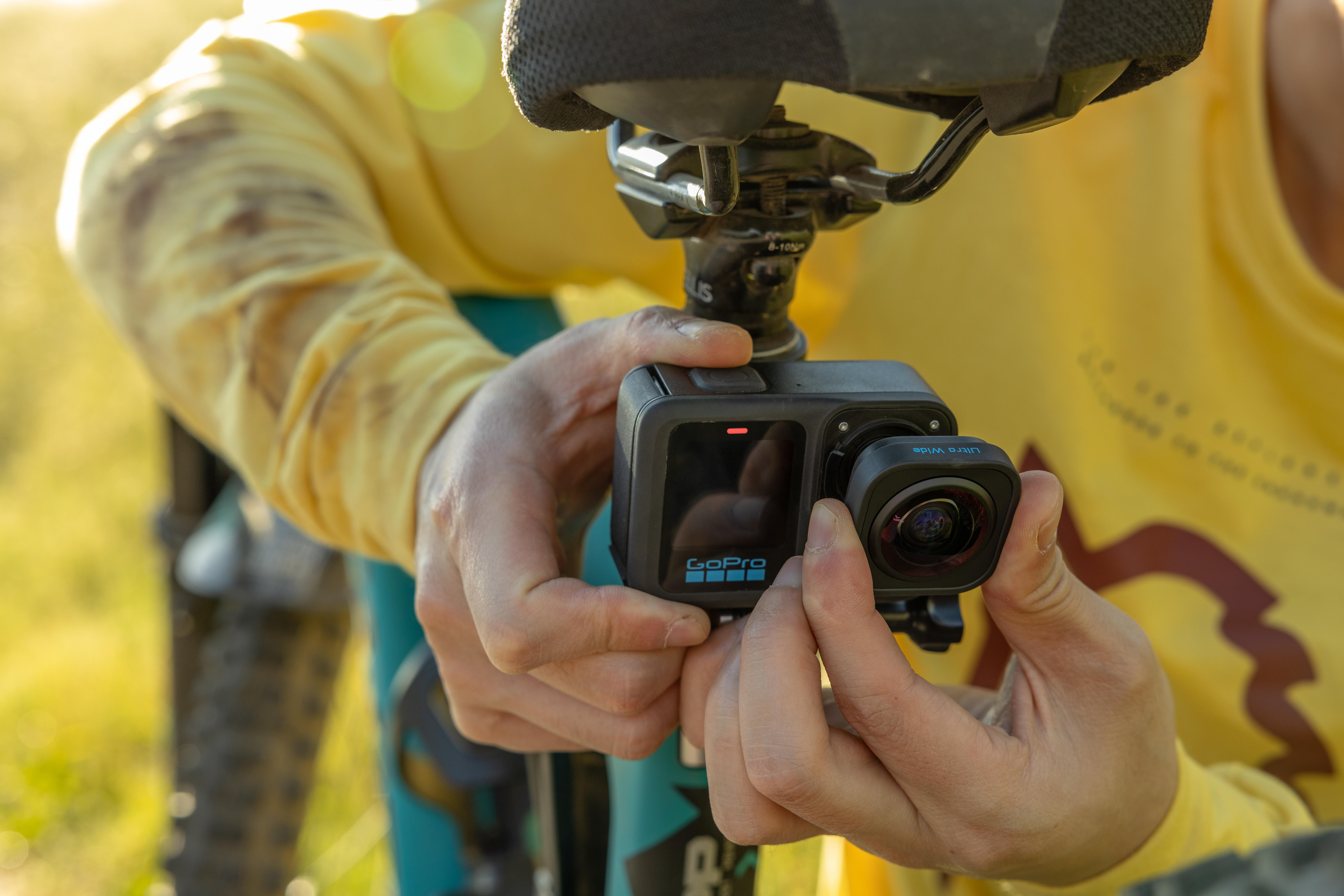 Eine Person hält eine GoPro-Kamera, die an einem Fahrradsitz befestigt ist. Die Person trägt ein gelbes Hemd. Der Hintergrund ist verschwommen.